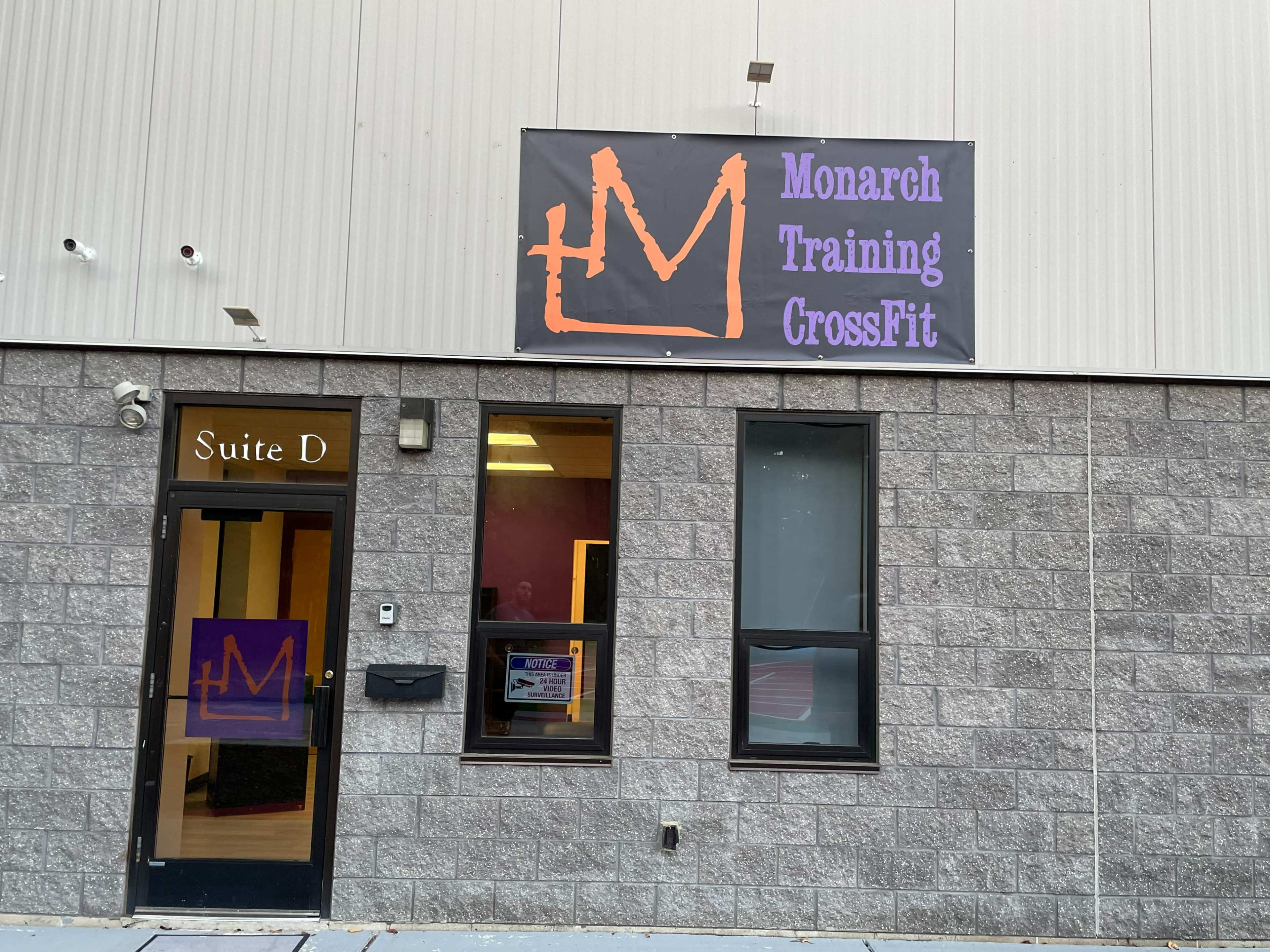 The entrance of a building labeled "Monarch Training CrossFit" with a large banner above the door and a sign indicating "Suite D."