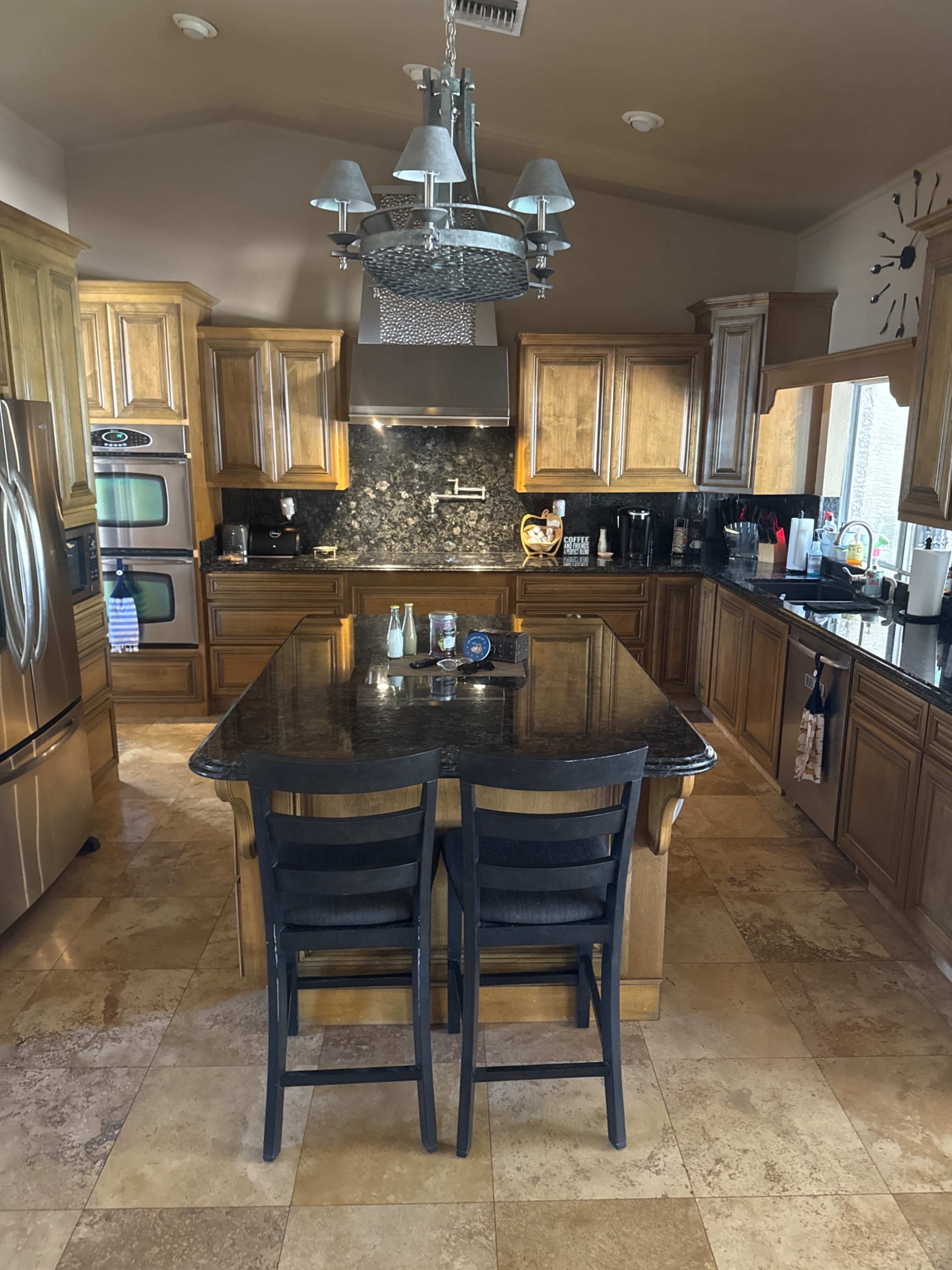 The image shows a spacious kitchen with wooden cabinetry, a large island in the center, and modern appliances, including a stainless steel refrigerator.