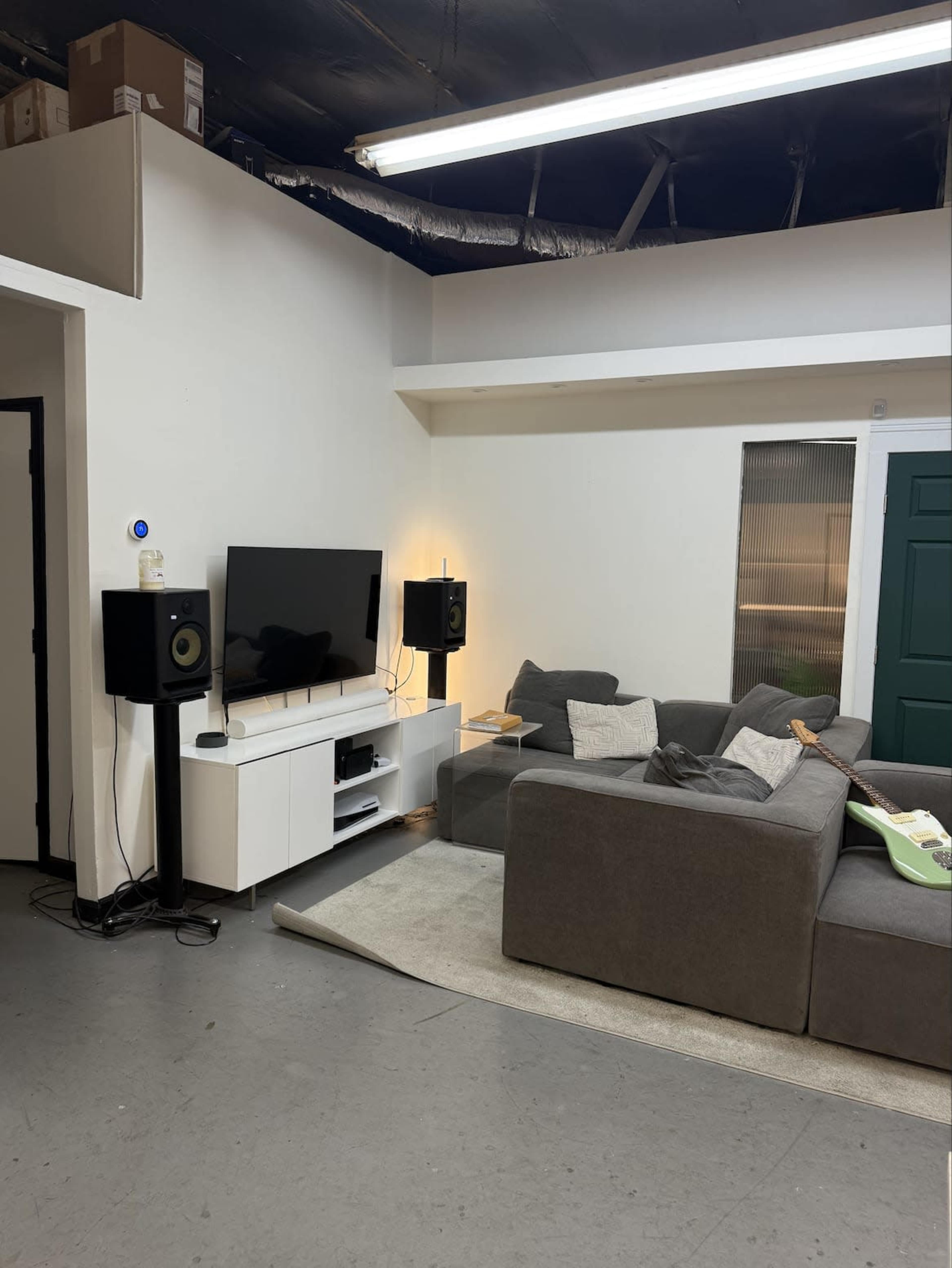 The image shows a modern living space with a gray sectional sofa, a white media console under a flat-screen TV, and two black speakers on either side.