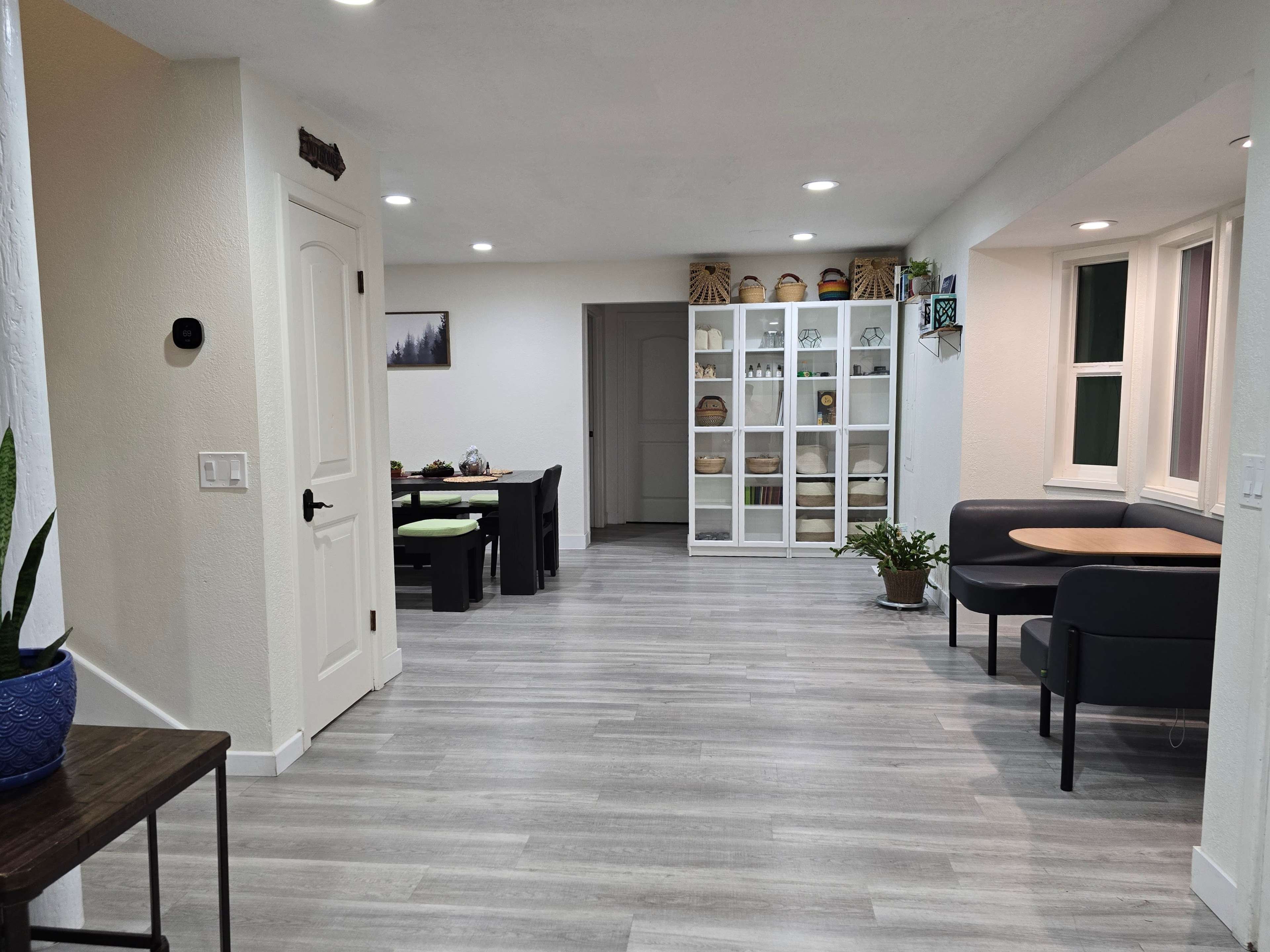 The image shows a modern interior space with a hallway leading to a dining area and a white storage cabinet filled with decorative items.