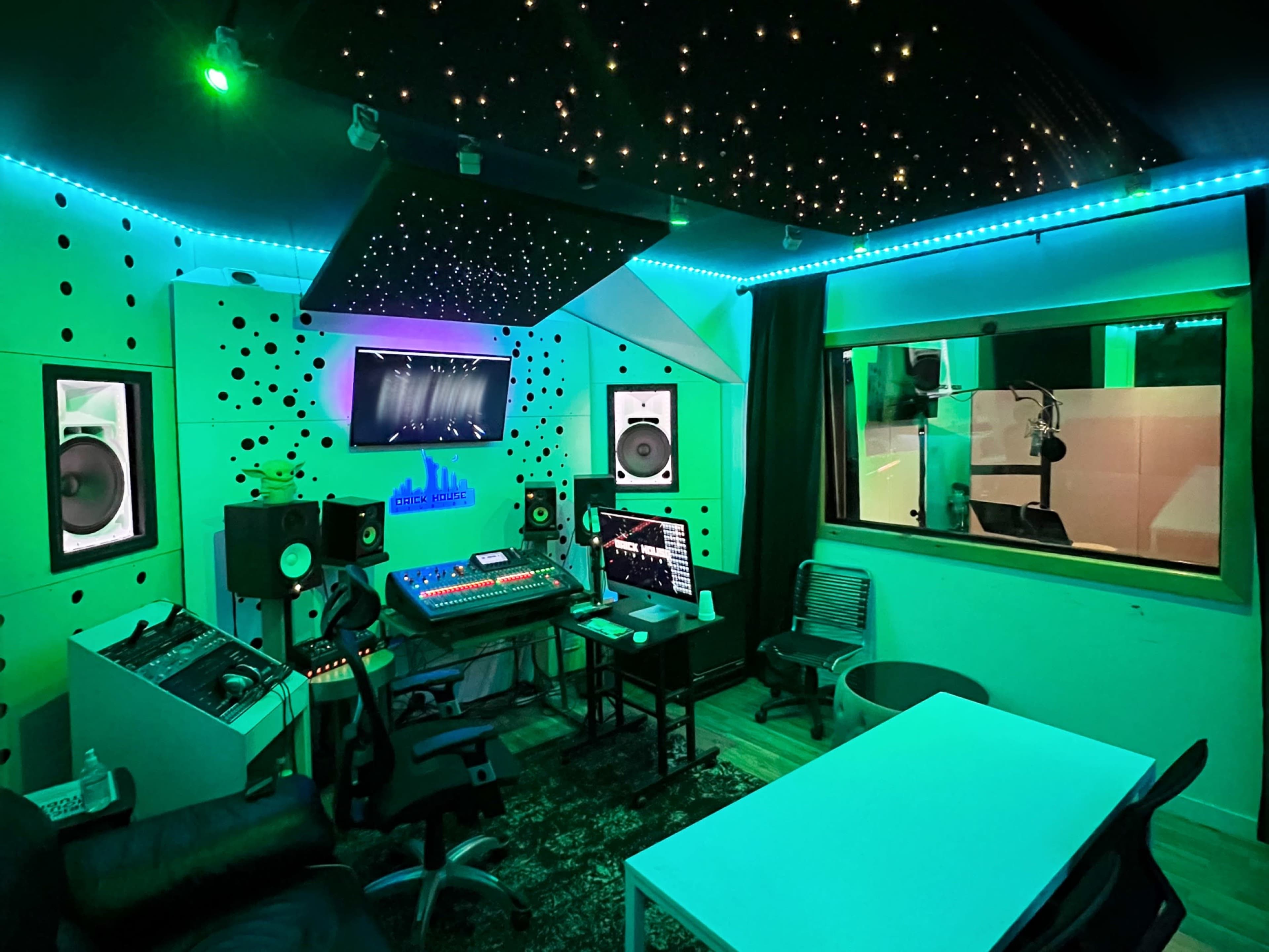 A modern recording studio with colorful LED lighting, sound equipment, and a vocal booth visible through a window.