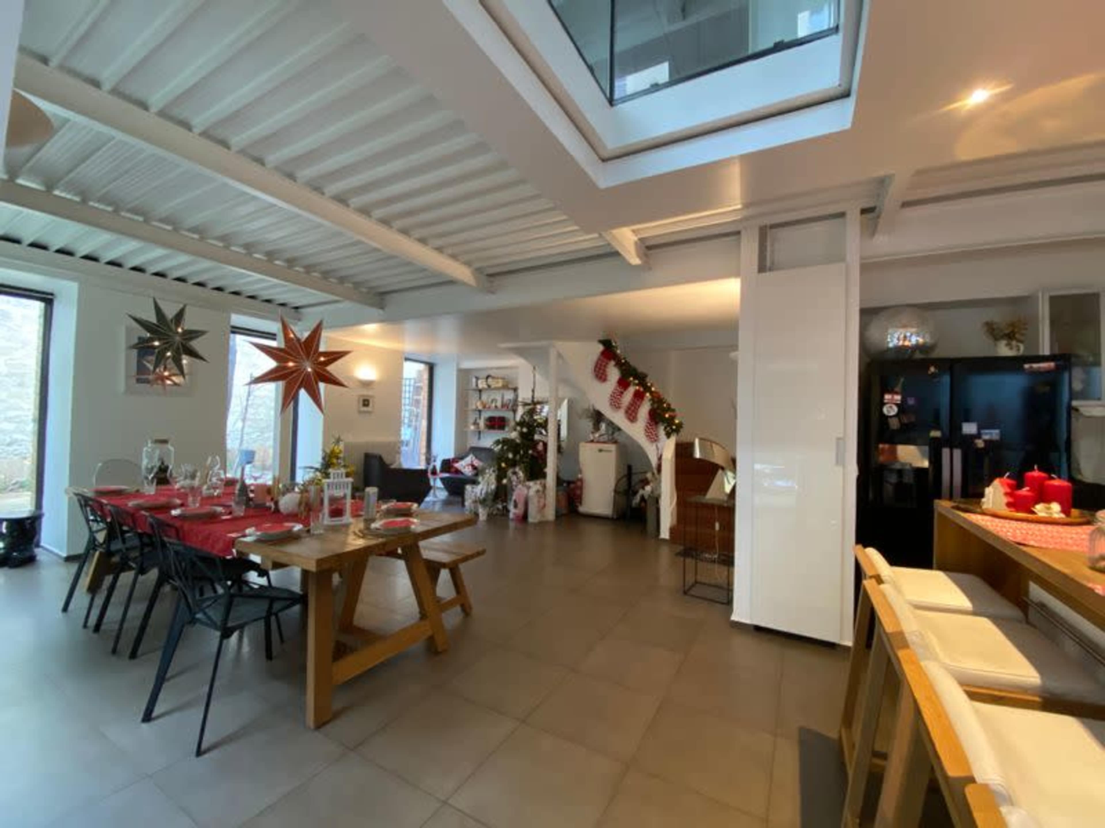 A modern, open-concept living space decorated for Christmas, featuring a dining area with a festive table setting and holiday decorations throughout the room.