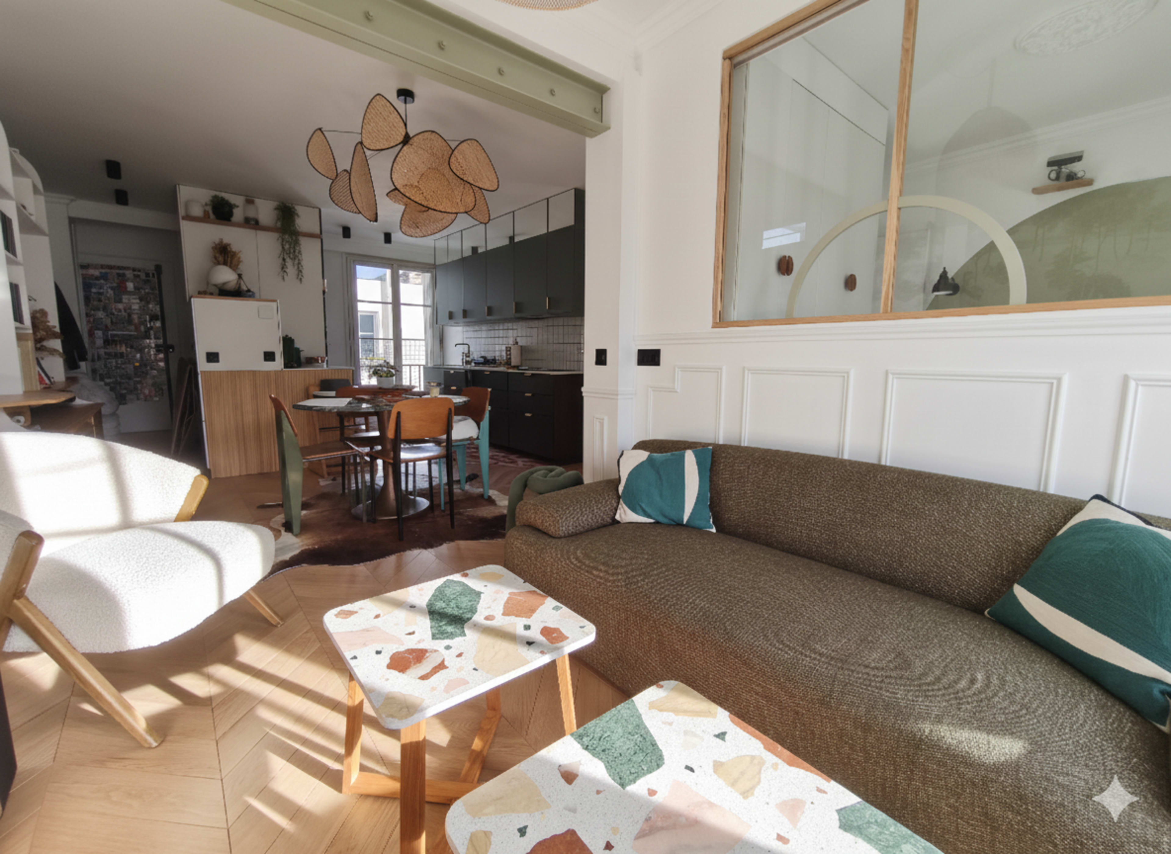 The image shows a modern living room with a sofa, a patterned coffee table, and a view into a dining area with a kitchen in the background.