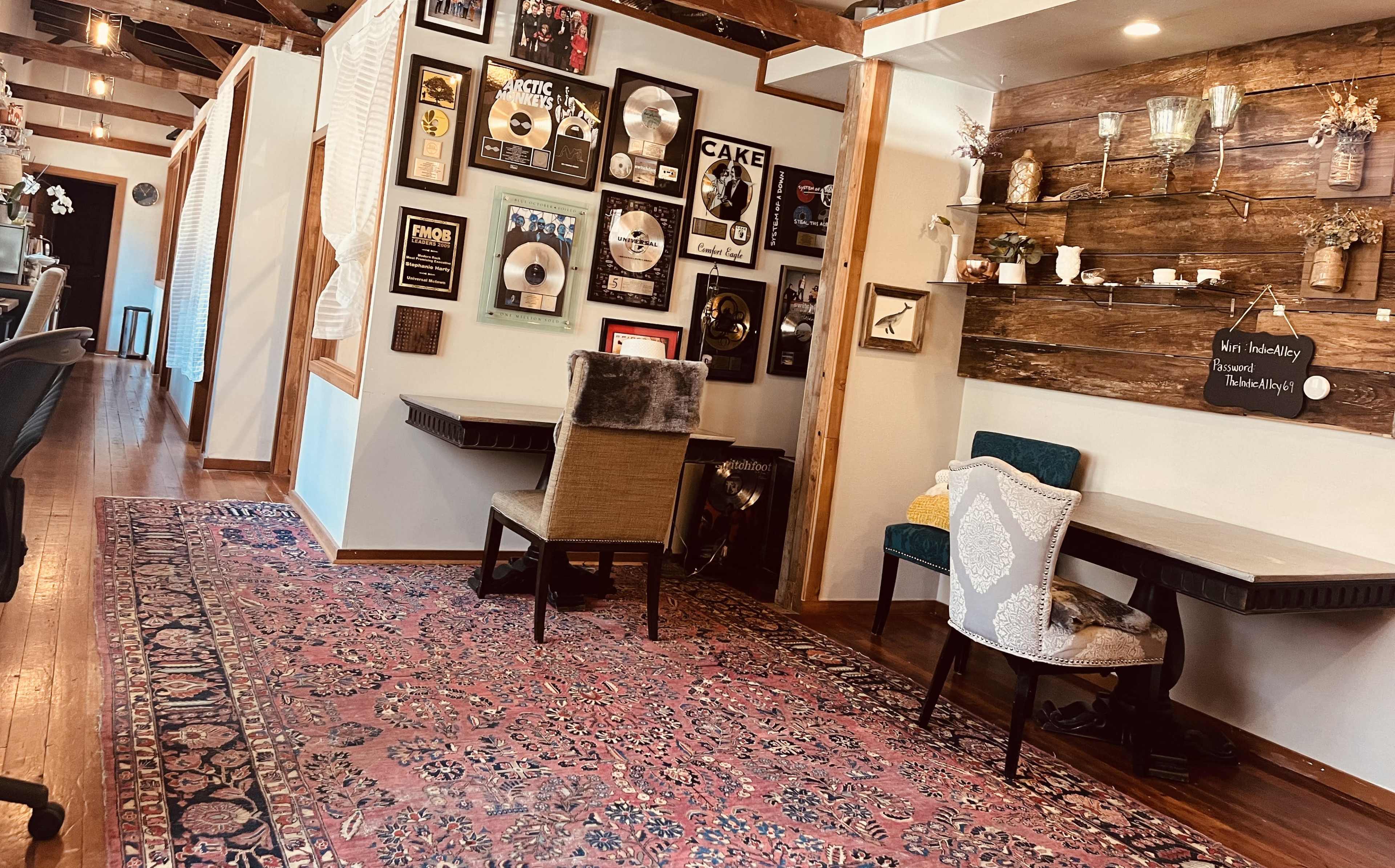 A hallway adorned with music awards on the walls, a patterned rug on the wooden floor, and small tables with chairs on either side.