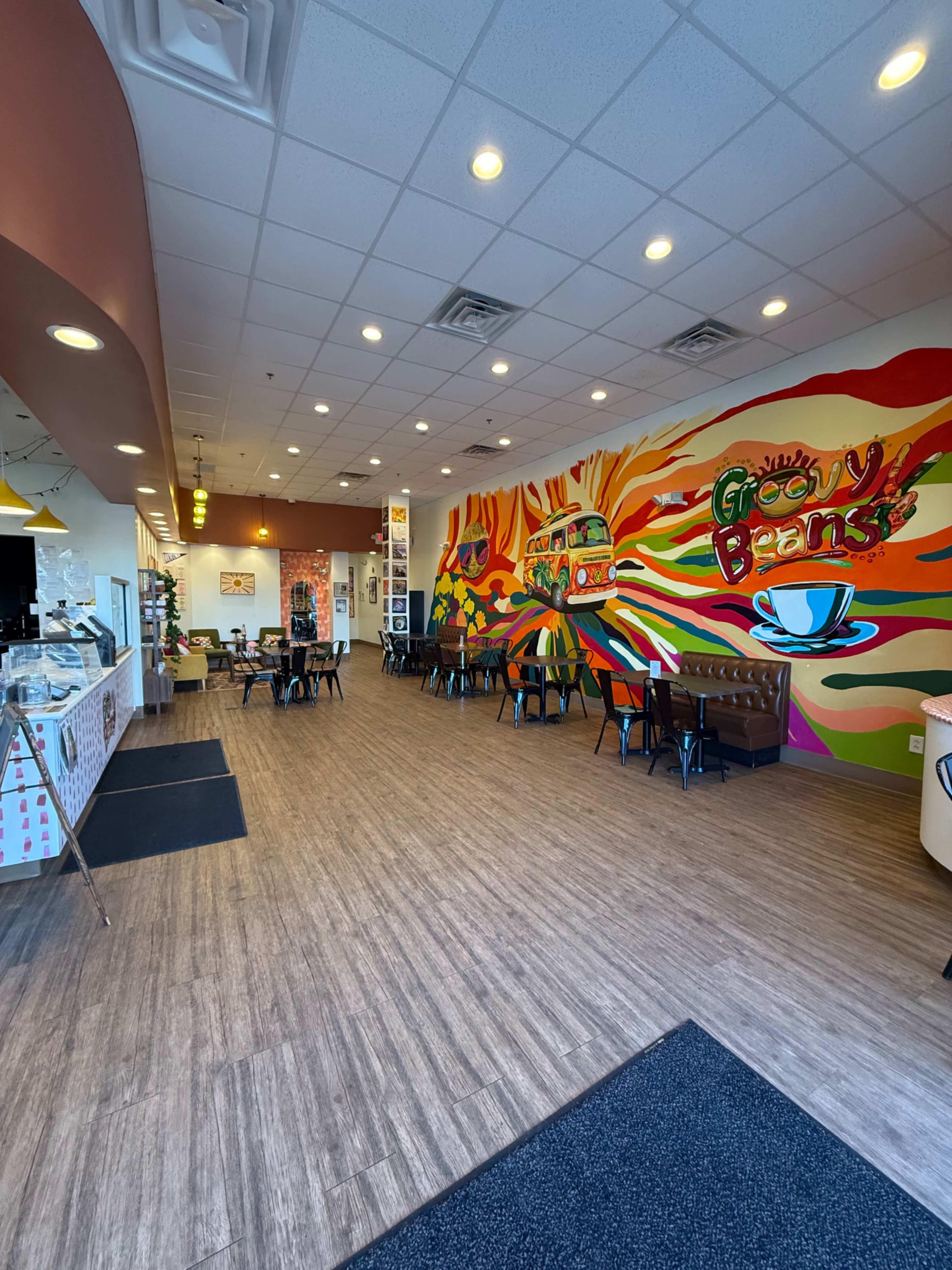 The image shows a vibrant café interior featuring colorful wall murals, wooden flooring, and tables arranged for dining.