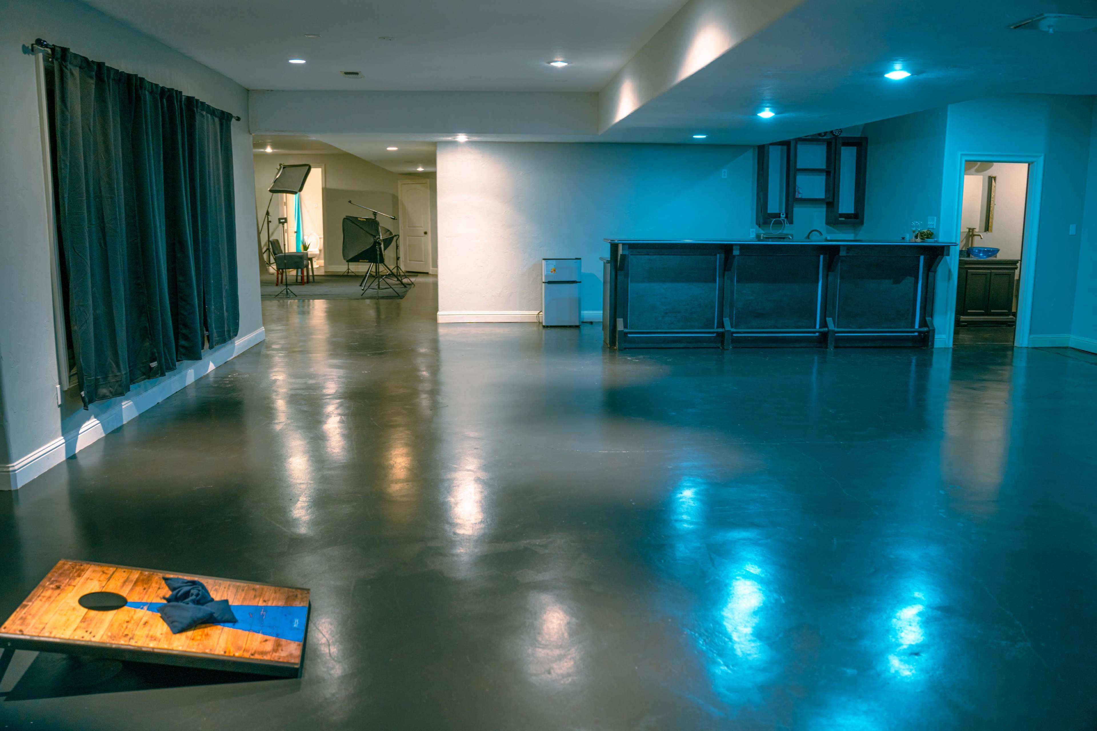 A spacious room with polished dark floors, a bar area in the back, and a cornhole game on the left.