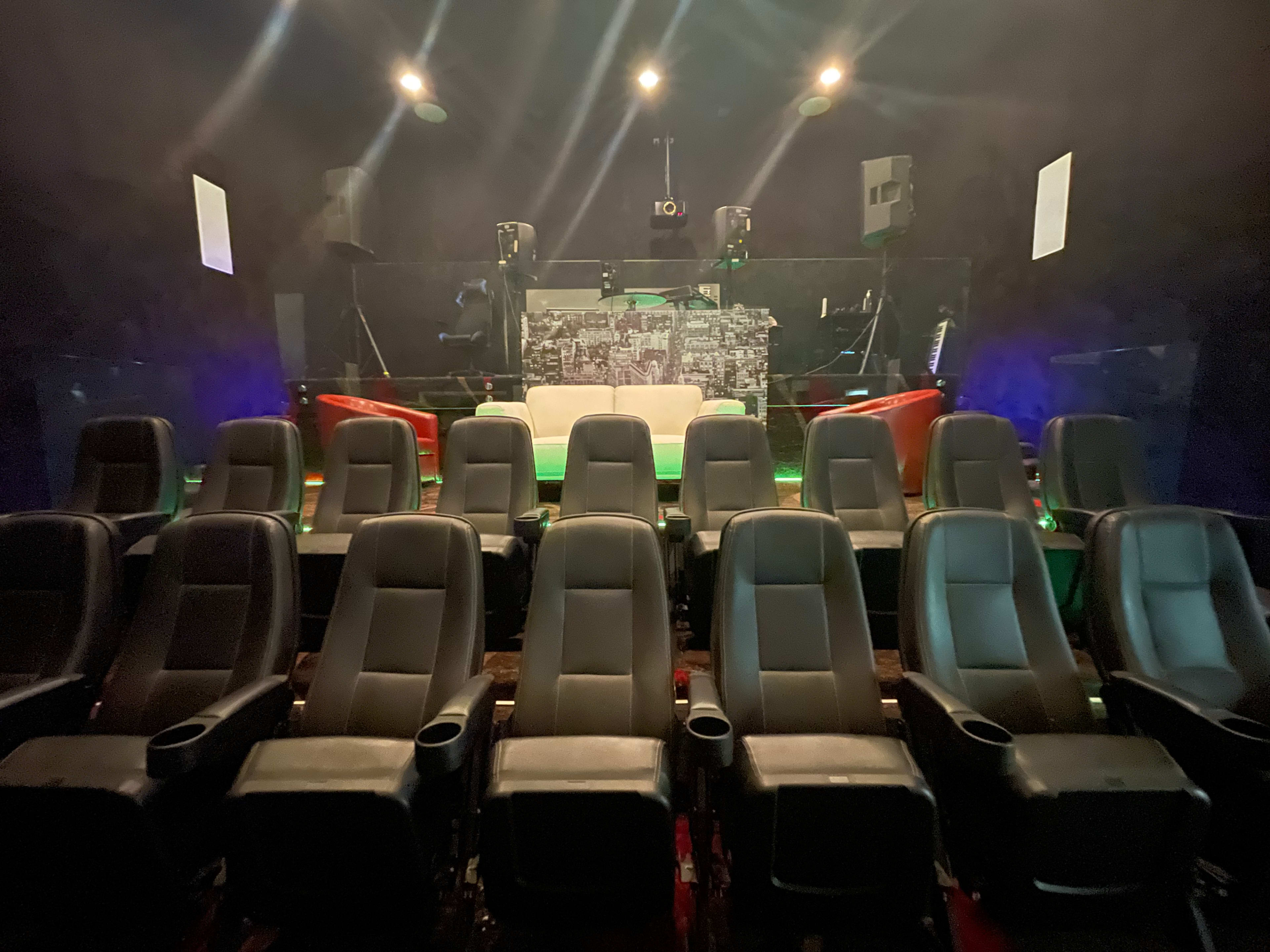 A row of black cinema chairs facing a blank screen in a dimly lit theater.
