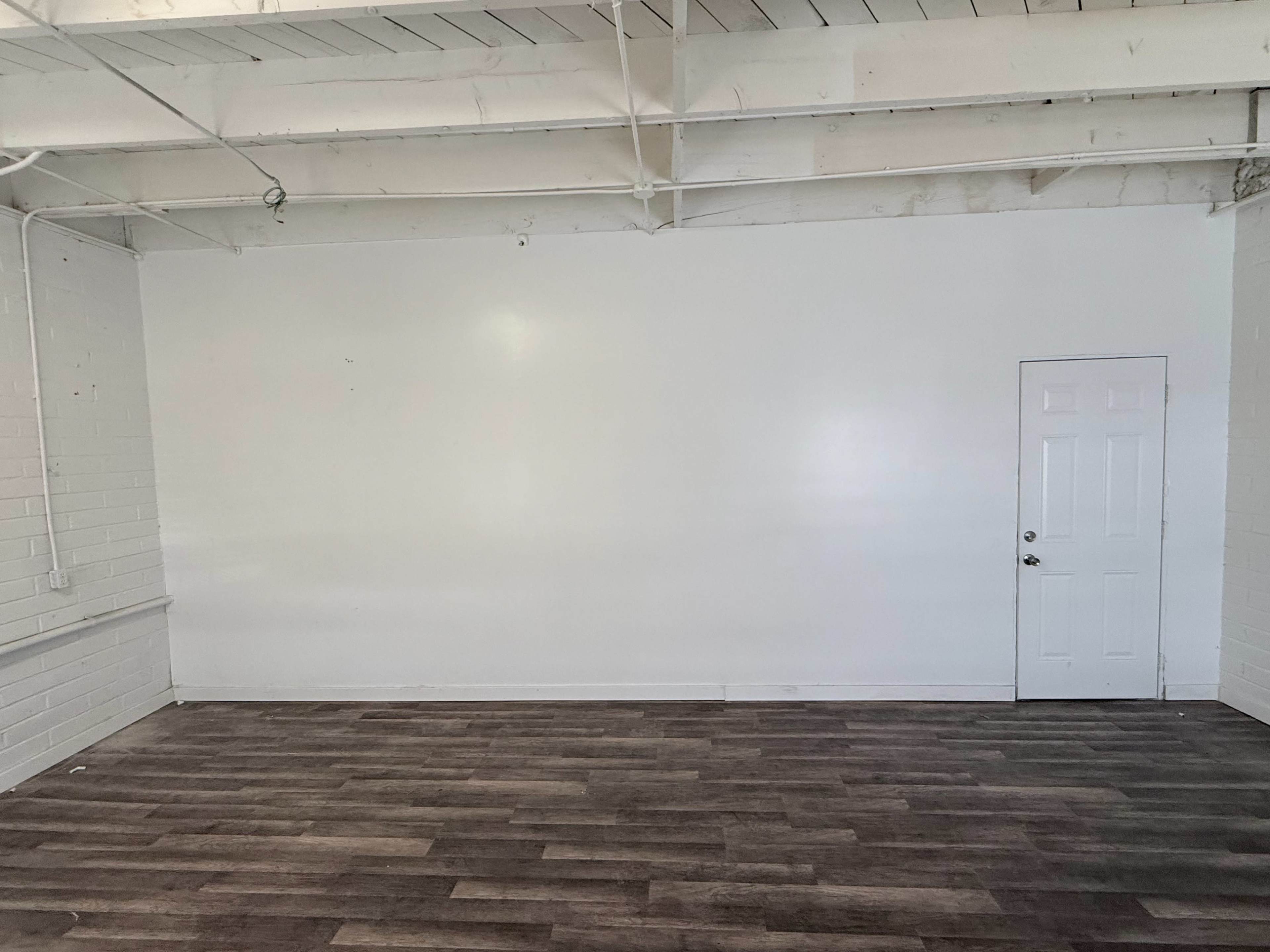 The image shows a bare room with white walls, a wooden floor, and a single door on the right side.