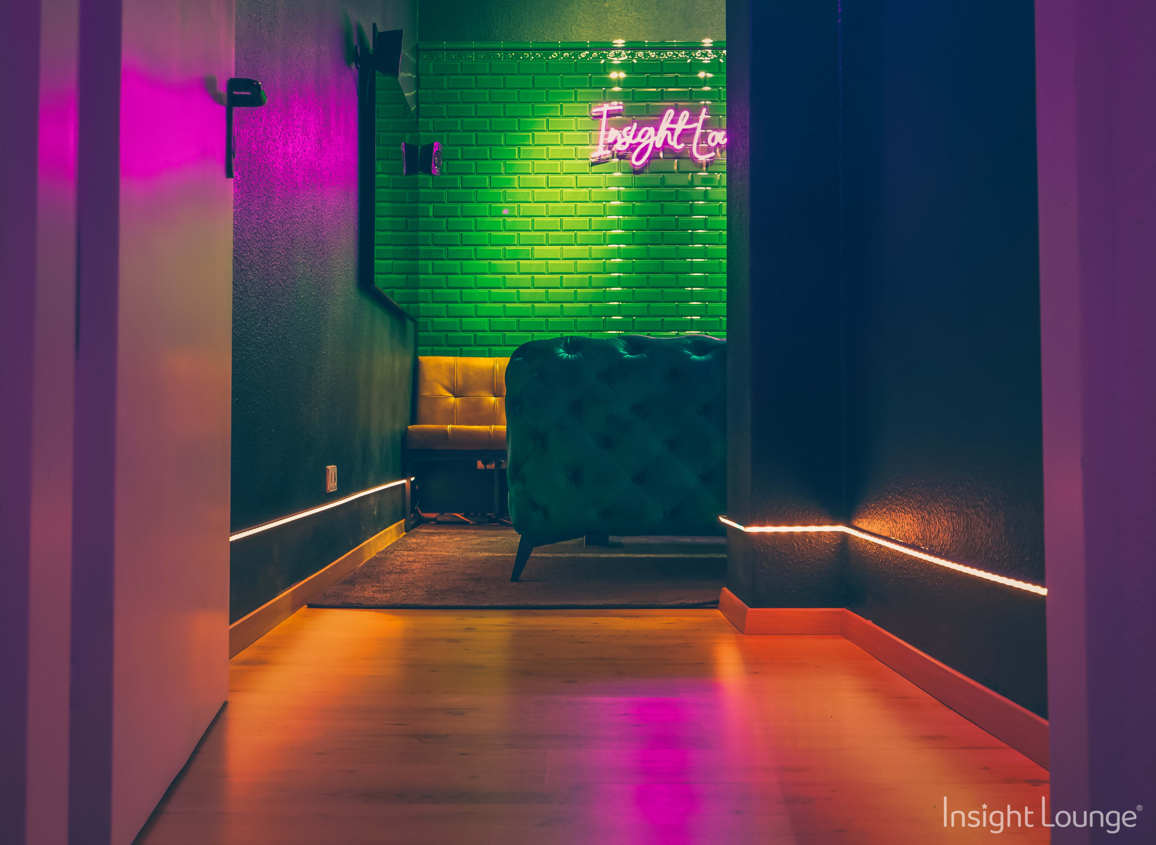 A vibrant lounge area with green brick walls, a yellow tufted couch, and neon lighting illuminating the space.