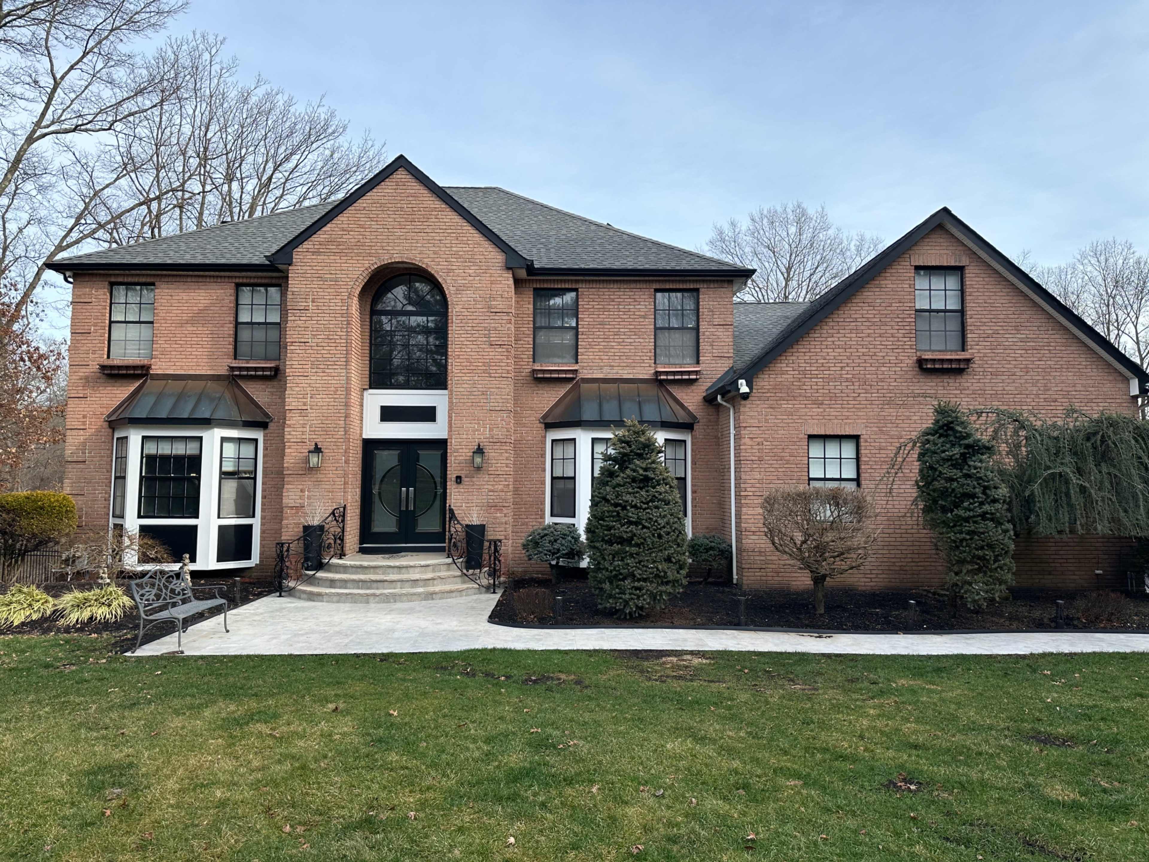 A two-story brick house with a central entrance flanked by large windows and landscaped front yard features.