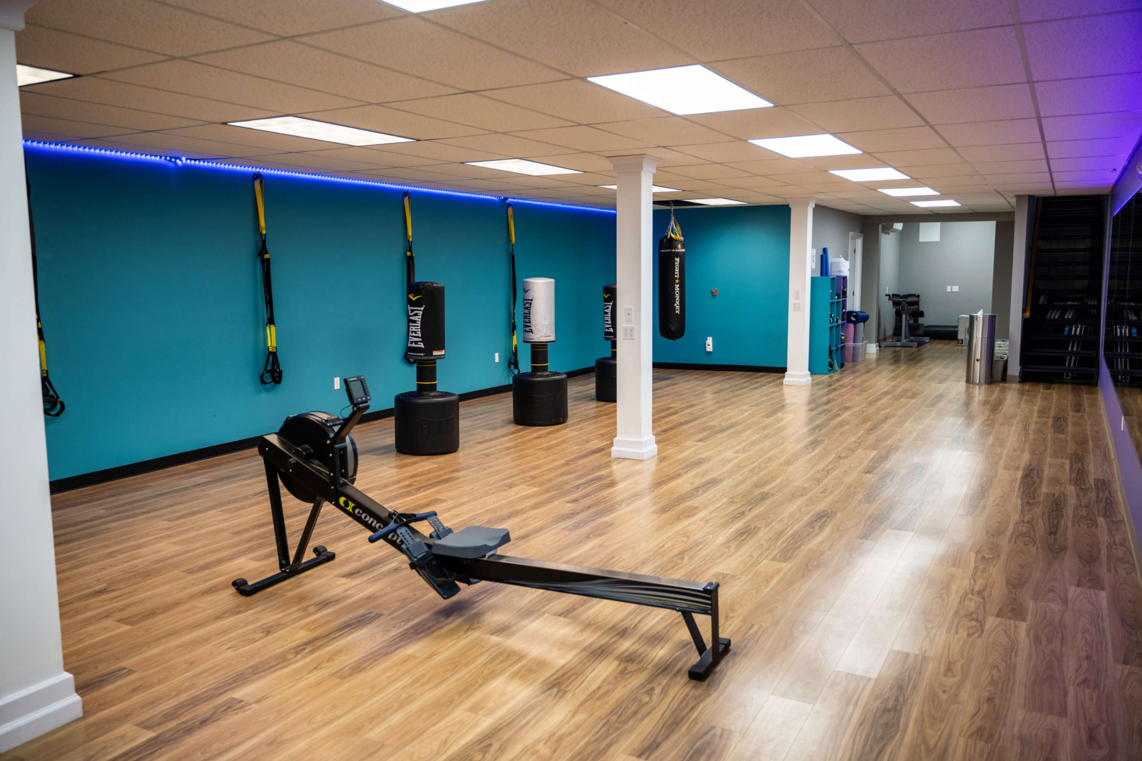 A fitness studio with wooden flooring, fitness equipment including a rowing machine and punching bags, and turquoise walls.