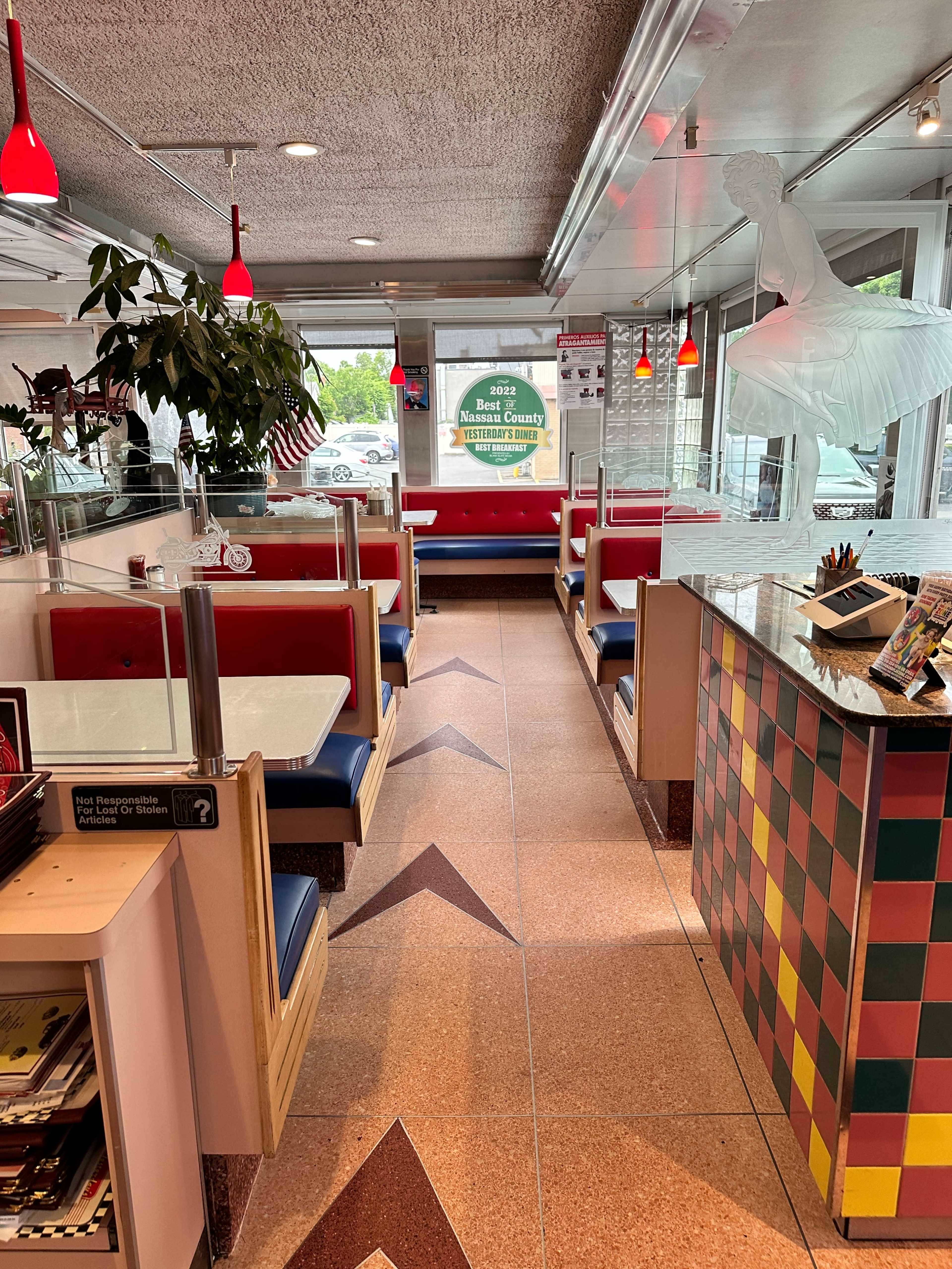 The interior of a diner with red and blue booths, a checkered counter, and a large white sculpture in the background.