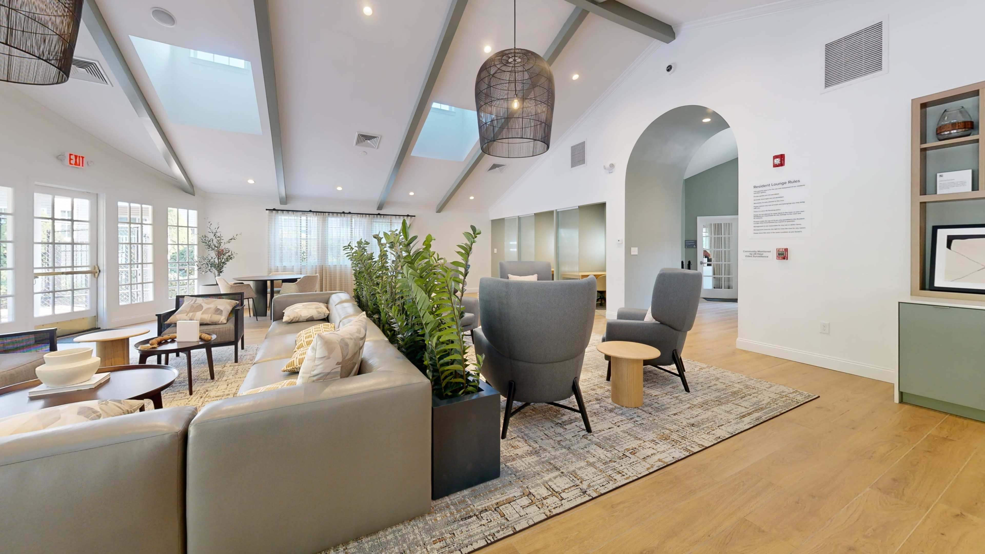 The image shows a modern lounge area with cozy seating, large windows above, and a potted plant in a stylish container.