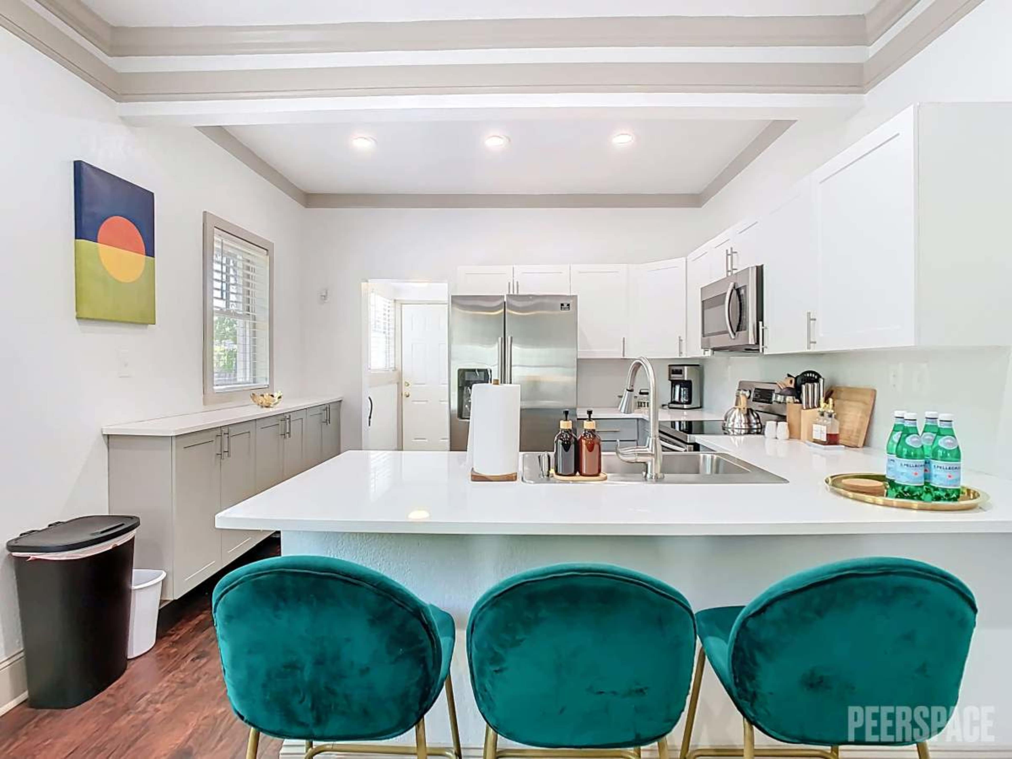 The image shows a modern kitchen with white cabinets, stainless steel appliances, and a central island with three green bar stools.