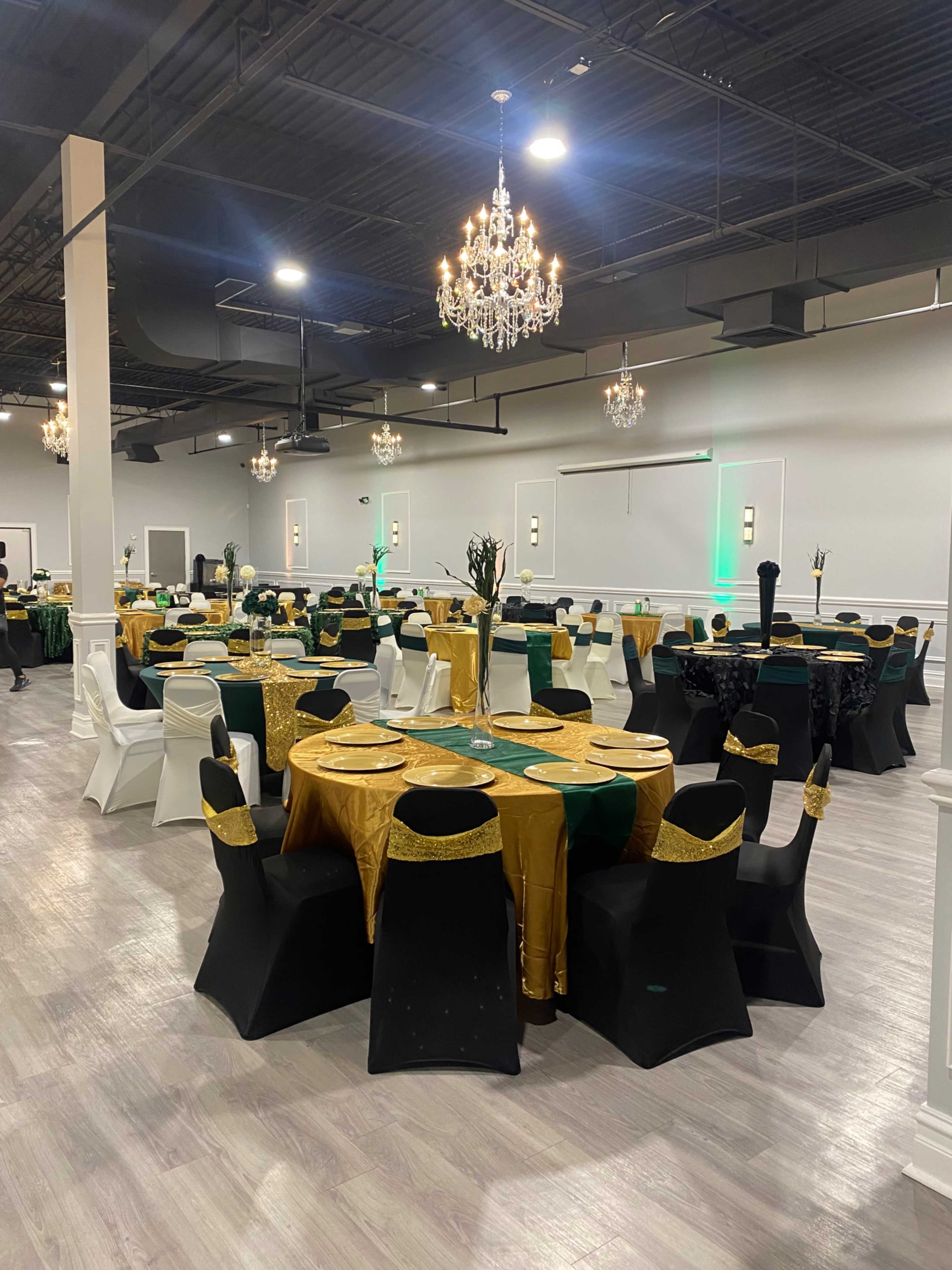 A banquet hall arranged for an event, featuring round tables with gold and green tablecloths, black chairs, and chandeliers overhead.