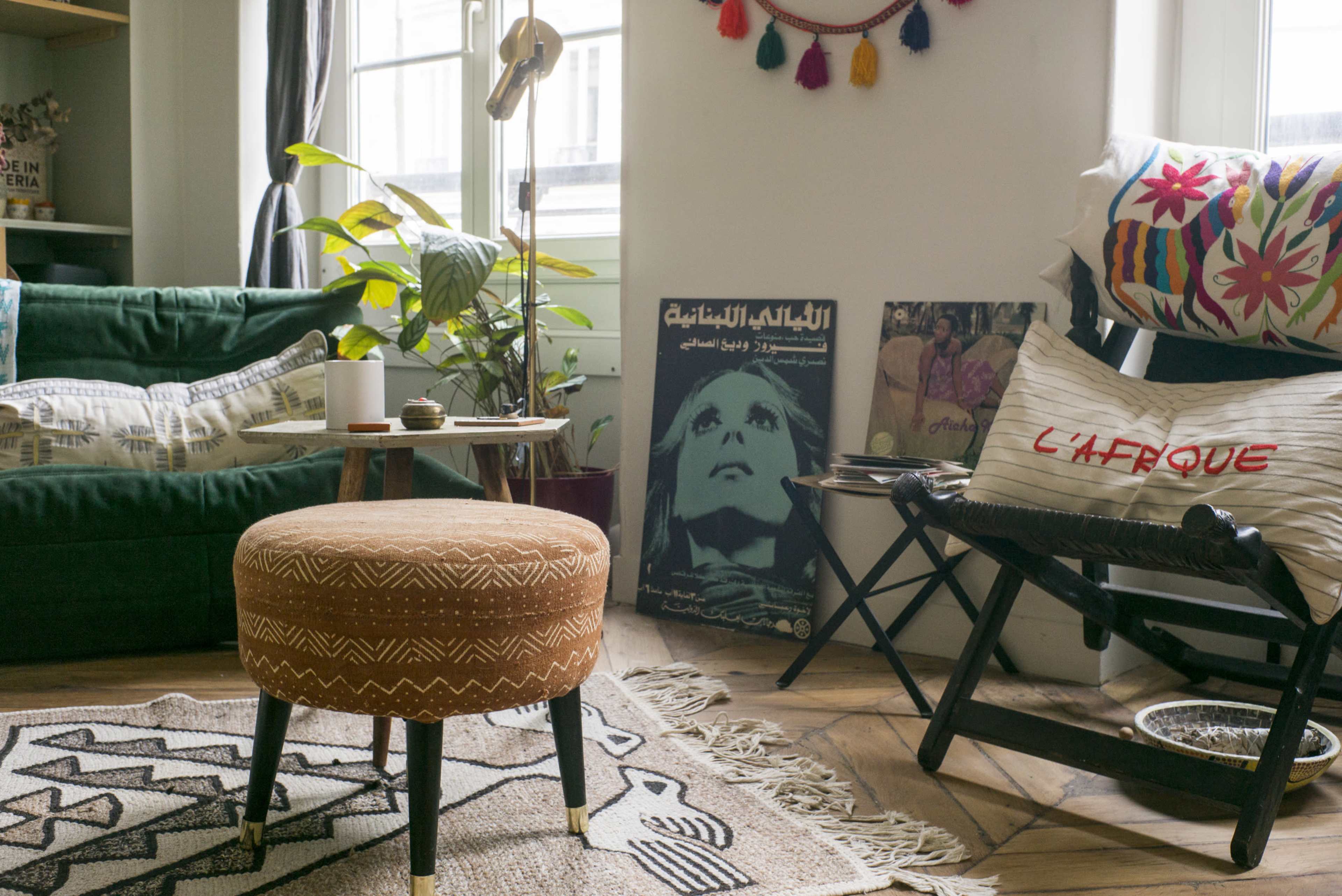 A cozy living room featuring a green sofa, a round ottoman, and a variety of decorative items, including plants and artwork on the walls.