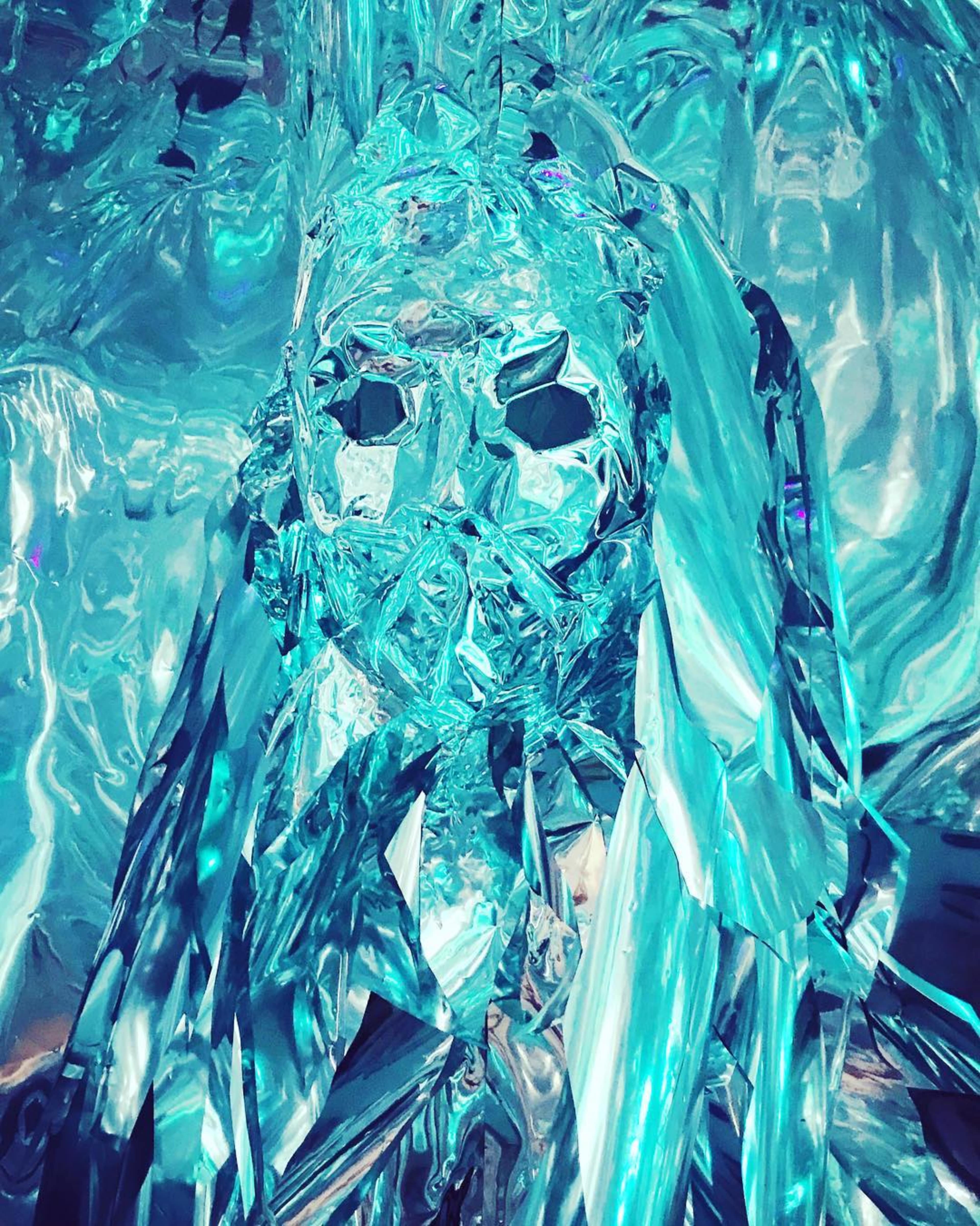 A figure seemingly made of crumpled, reflective blue material resembling a person obscured by layers of shiny, metallic fabric.