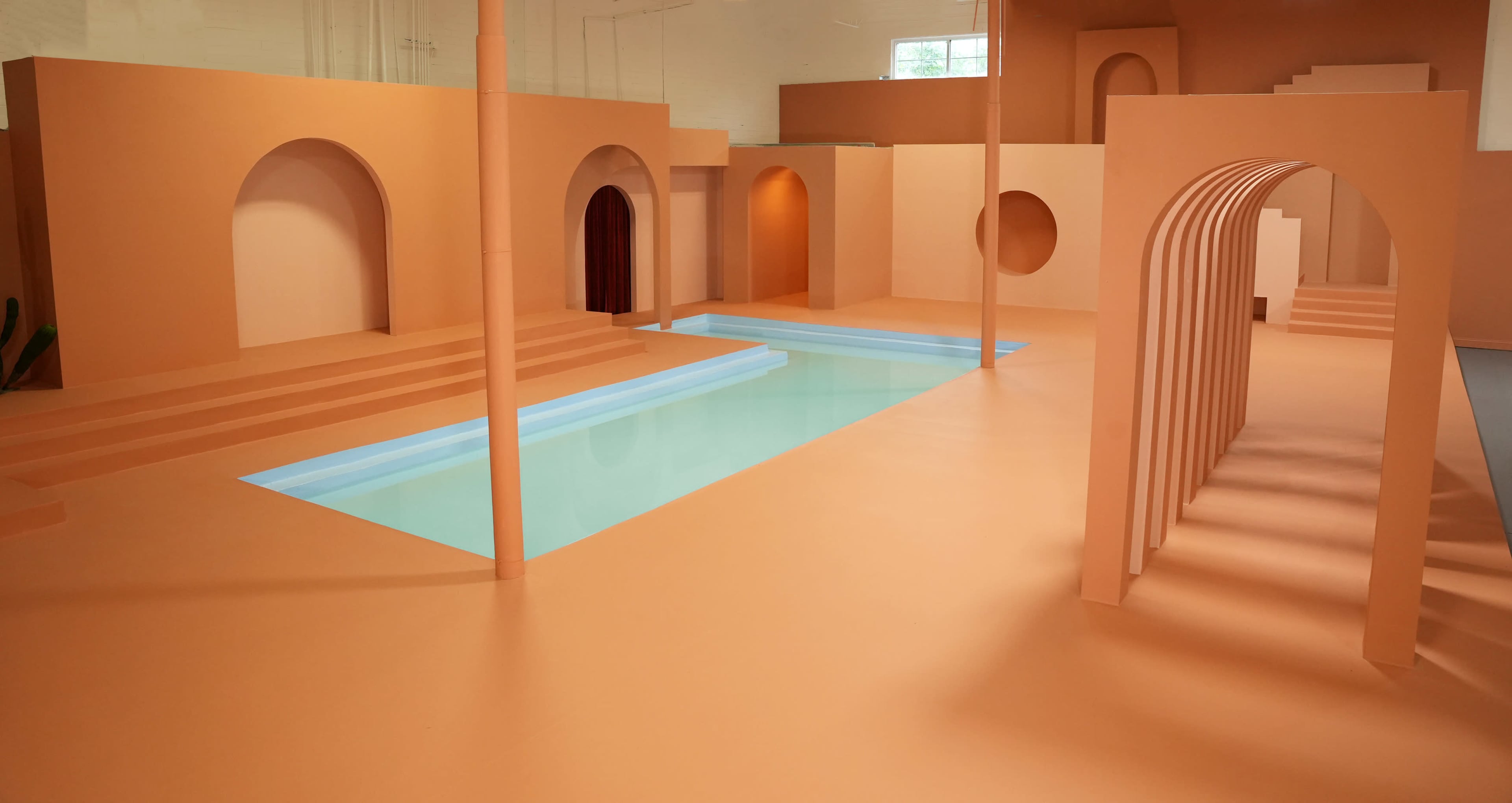 A modern interior space with an orange color scheme, featuring a swimming pool surrounded by curved architectural elements and steps.