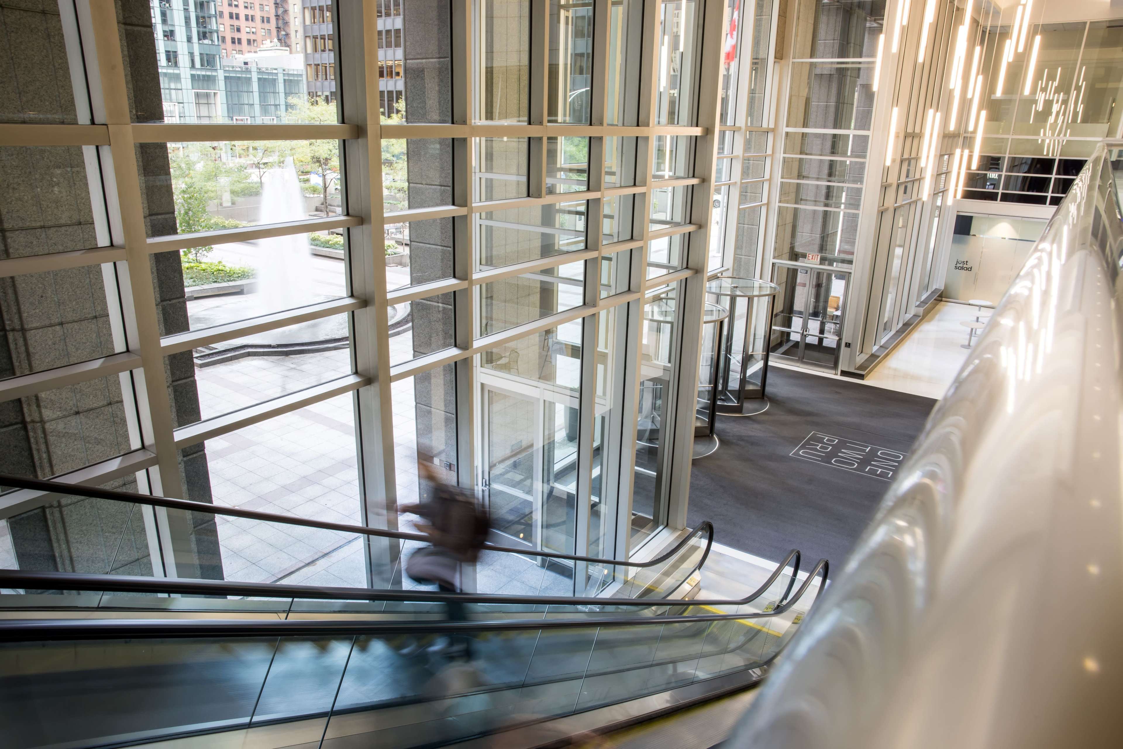 A person descends an escalator in a modern lobby filled with natural light and glass walls.