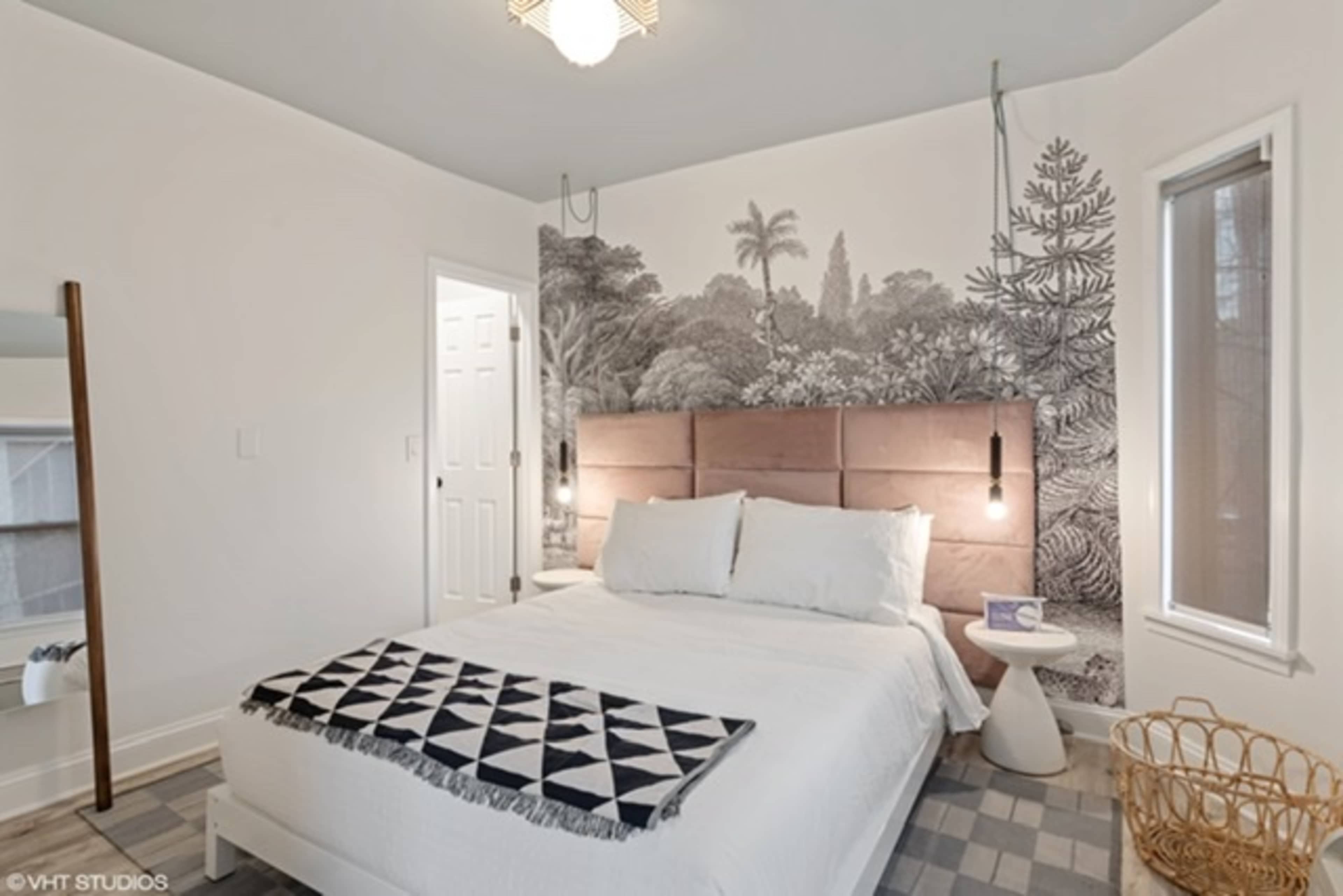 A modern bedroom features a large bed with a patterned throw, a textured wall mural, and minimalist decor.