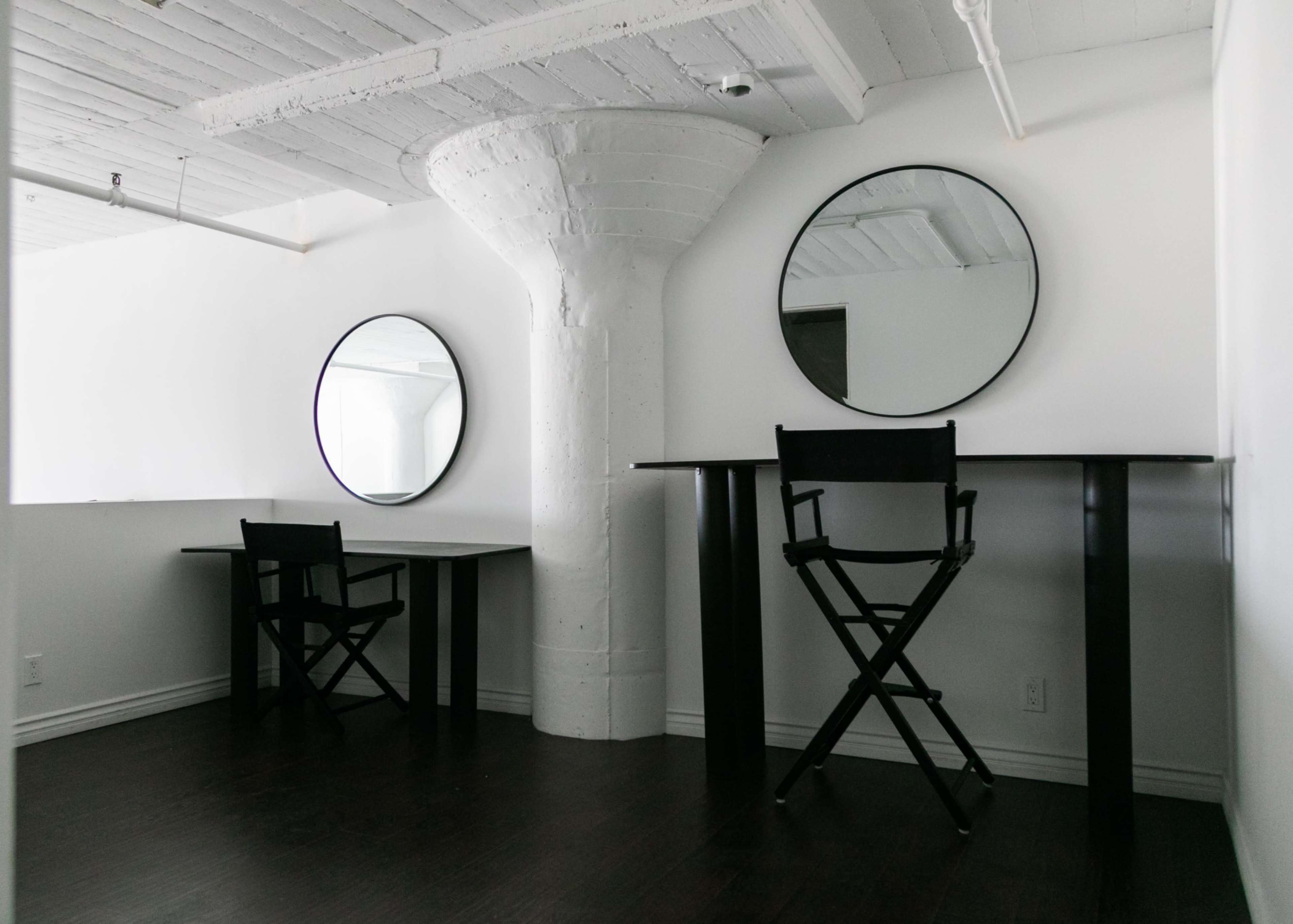 A minimalistic room with two round mirrors mounted on the wall above two black tables, separated by a white column.
