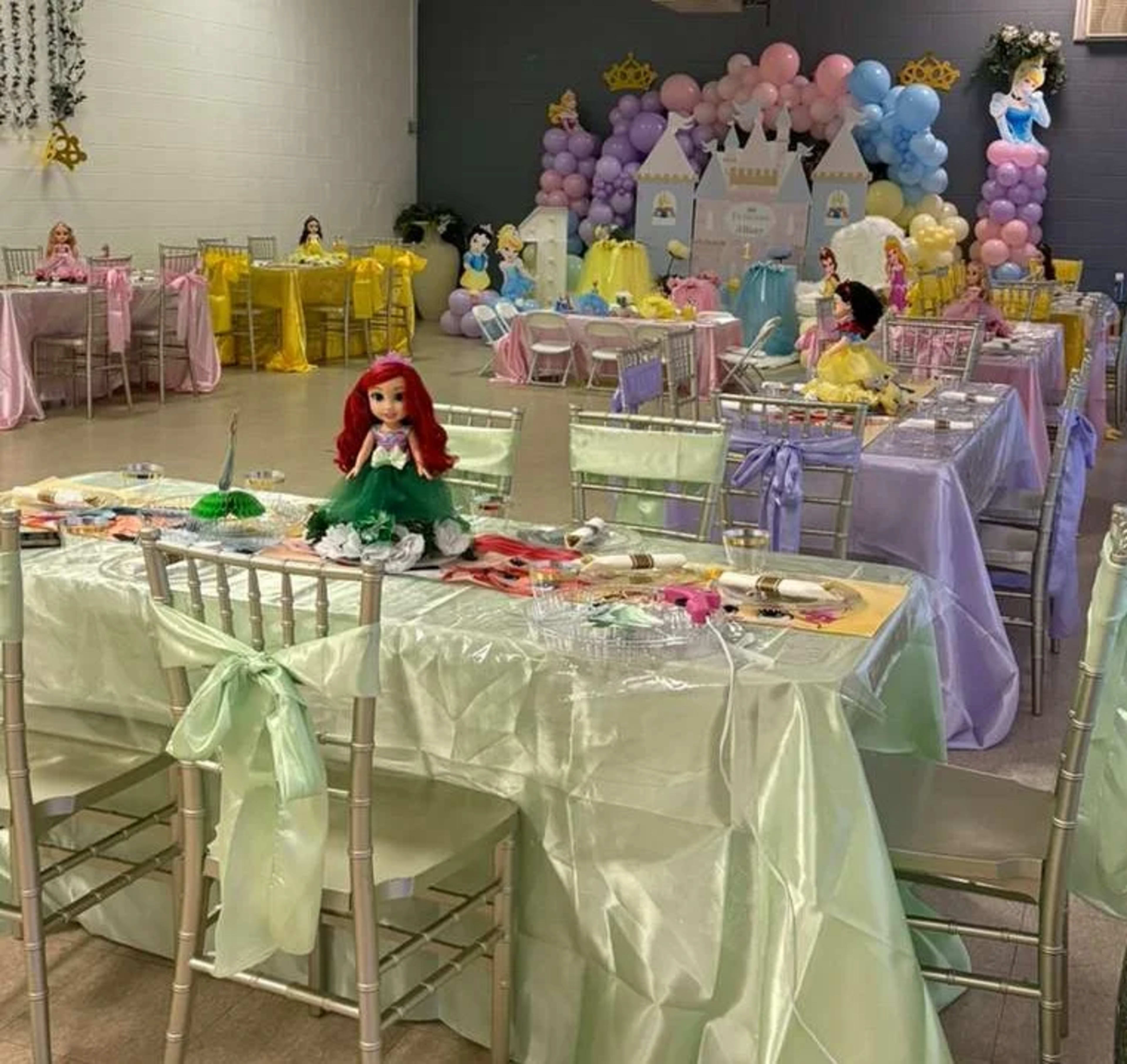 A colorful party room is set up with tables adorned in pastel colors, featuring princess decorations and dolls.