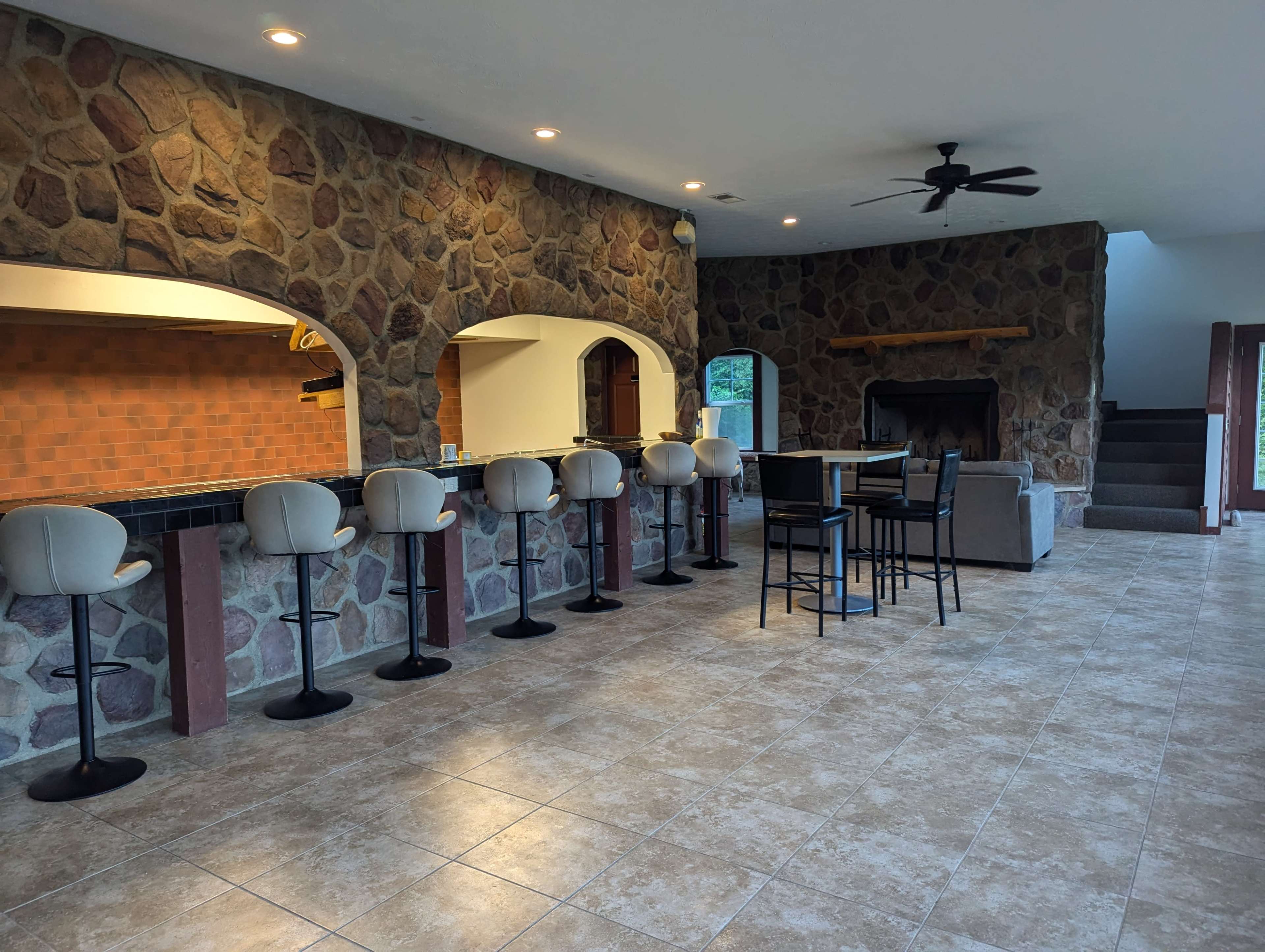 A spacious interior with a stone wall, a bar area with several stools, and a seating arrangement near a fireplace.