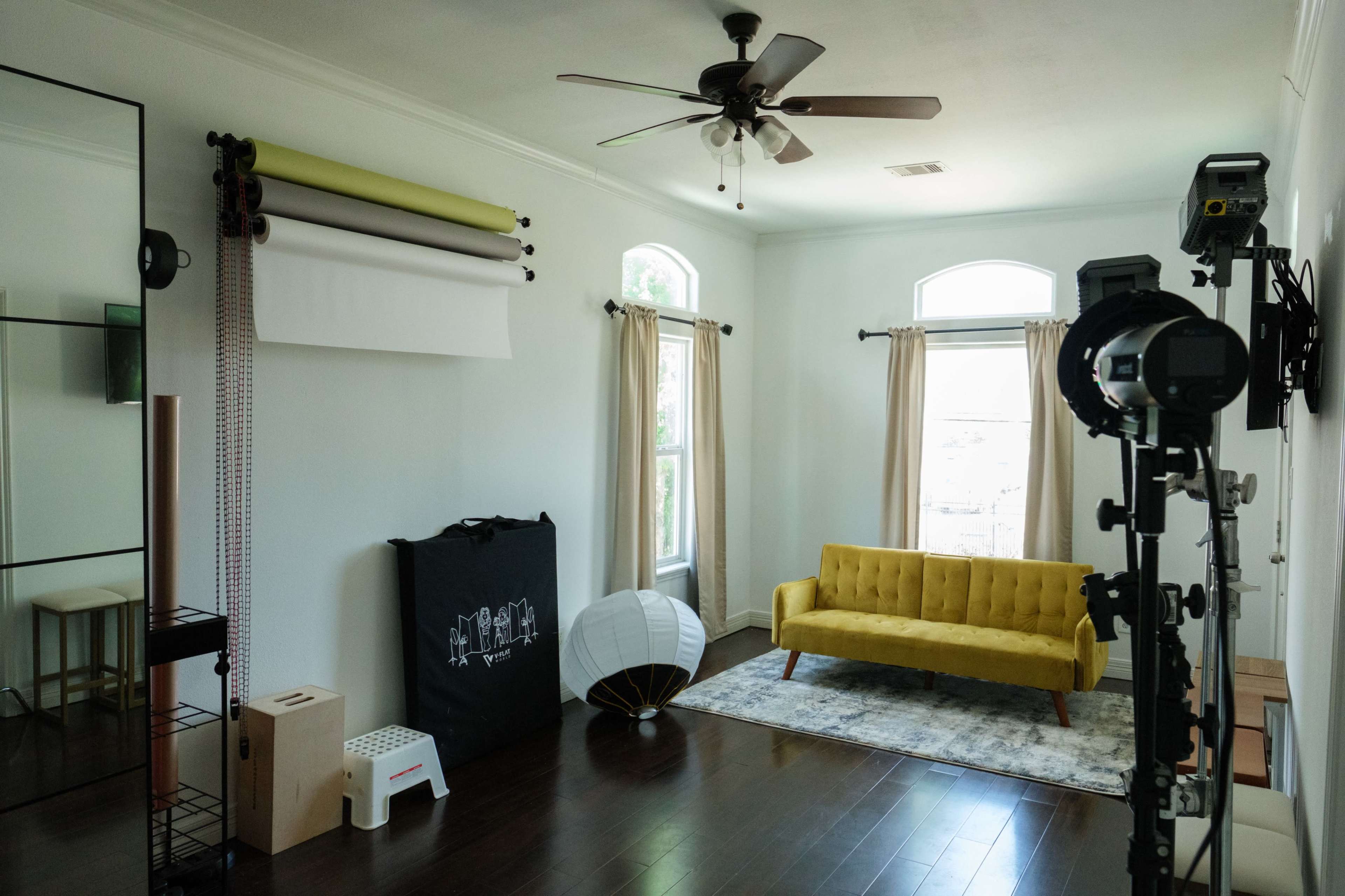 A well-lit room features a yellow couch, a decorative lamp, and photography equipment against the walls.