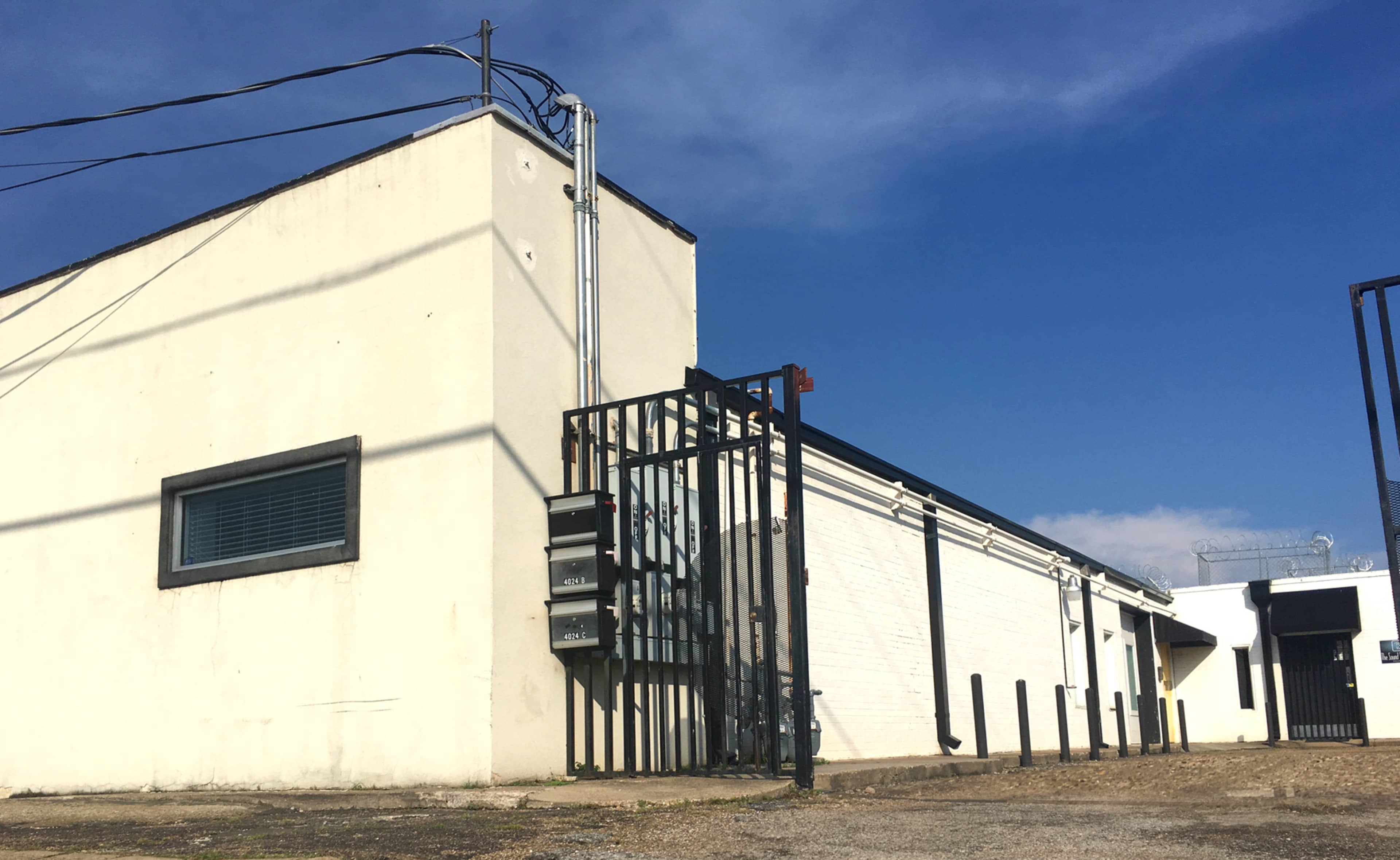 A white building with a gated entrance, surrounded by gravel and a clear blue sky.