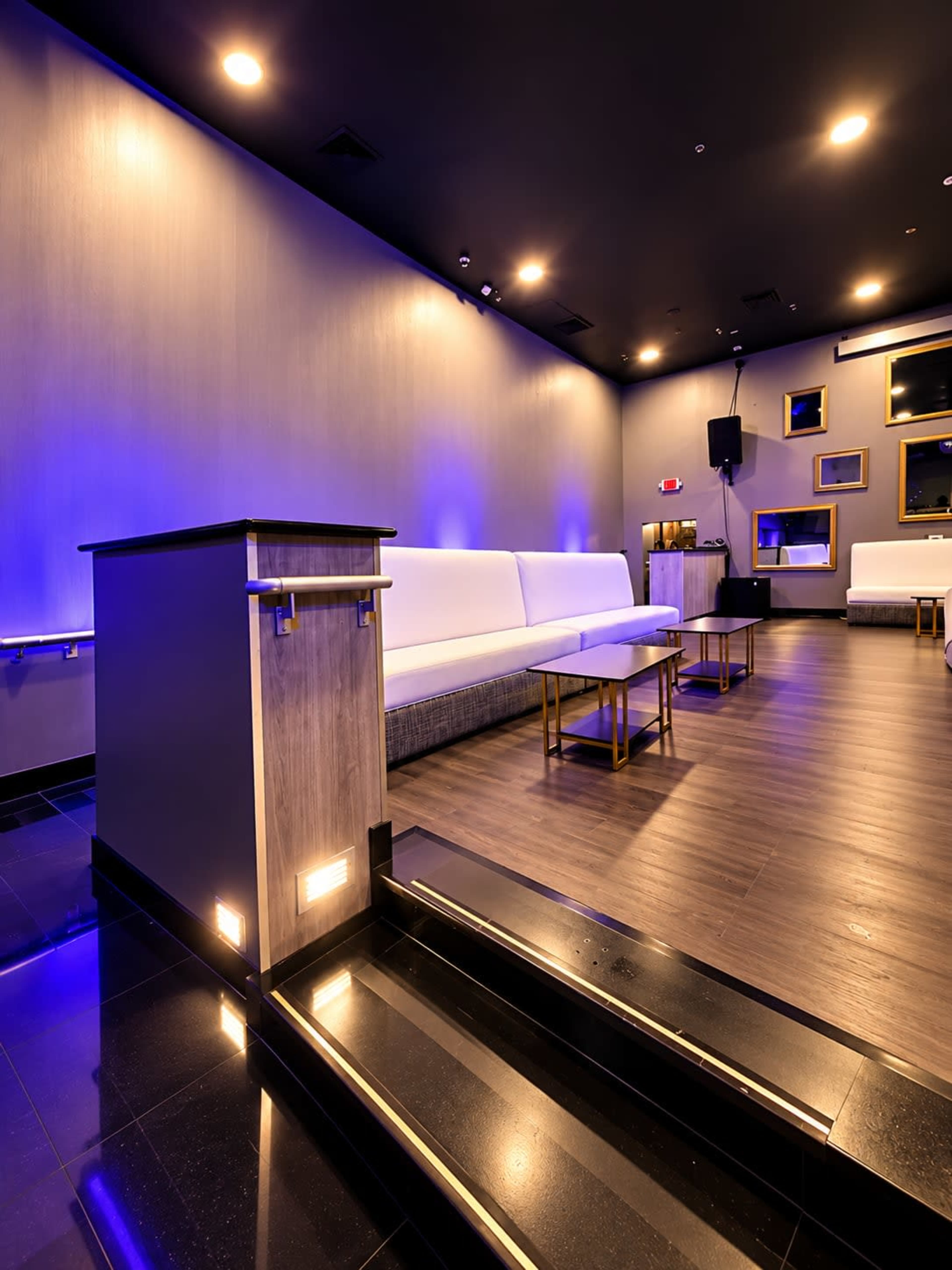 The image shows a modern lounge space with white couches, wooden tables, and blue ambient lighting.