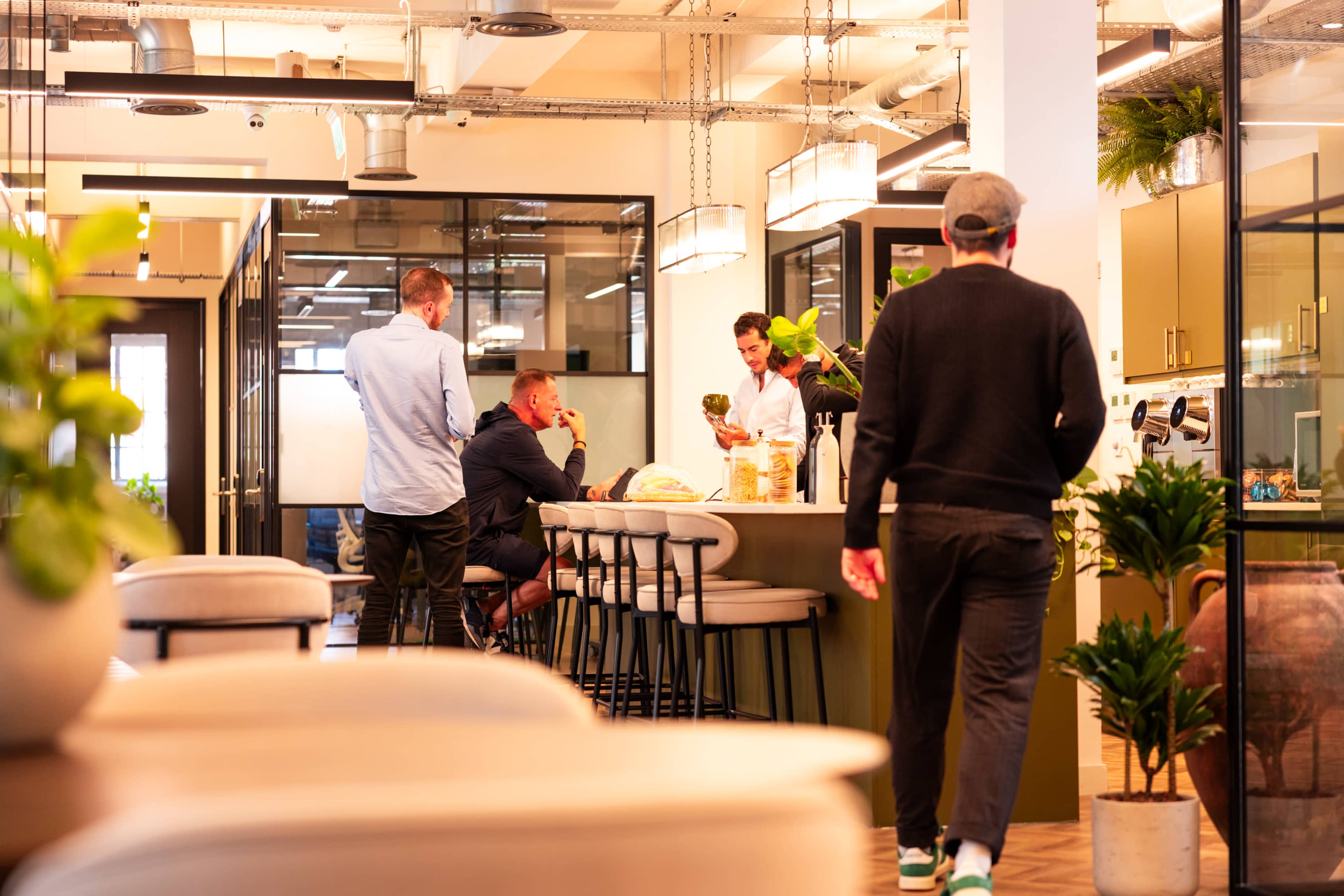 A group of people are socializing and preparing food in a modern kitchen area within an office space.