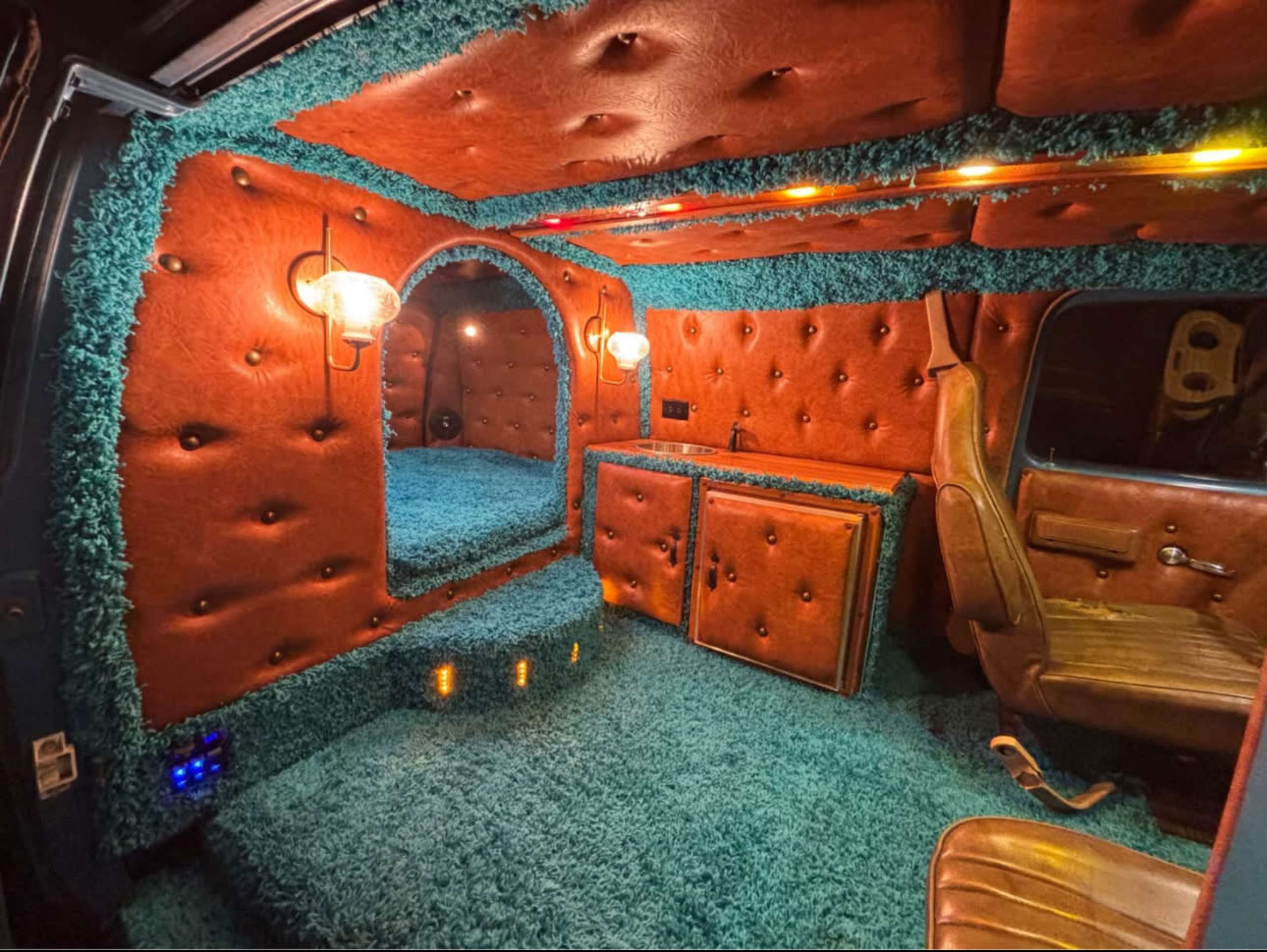 The interior of the vehicle features plush orange leather walls, a mirrored arch, and bright turquoise carpeting.
