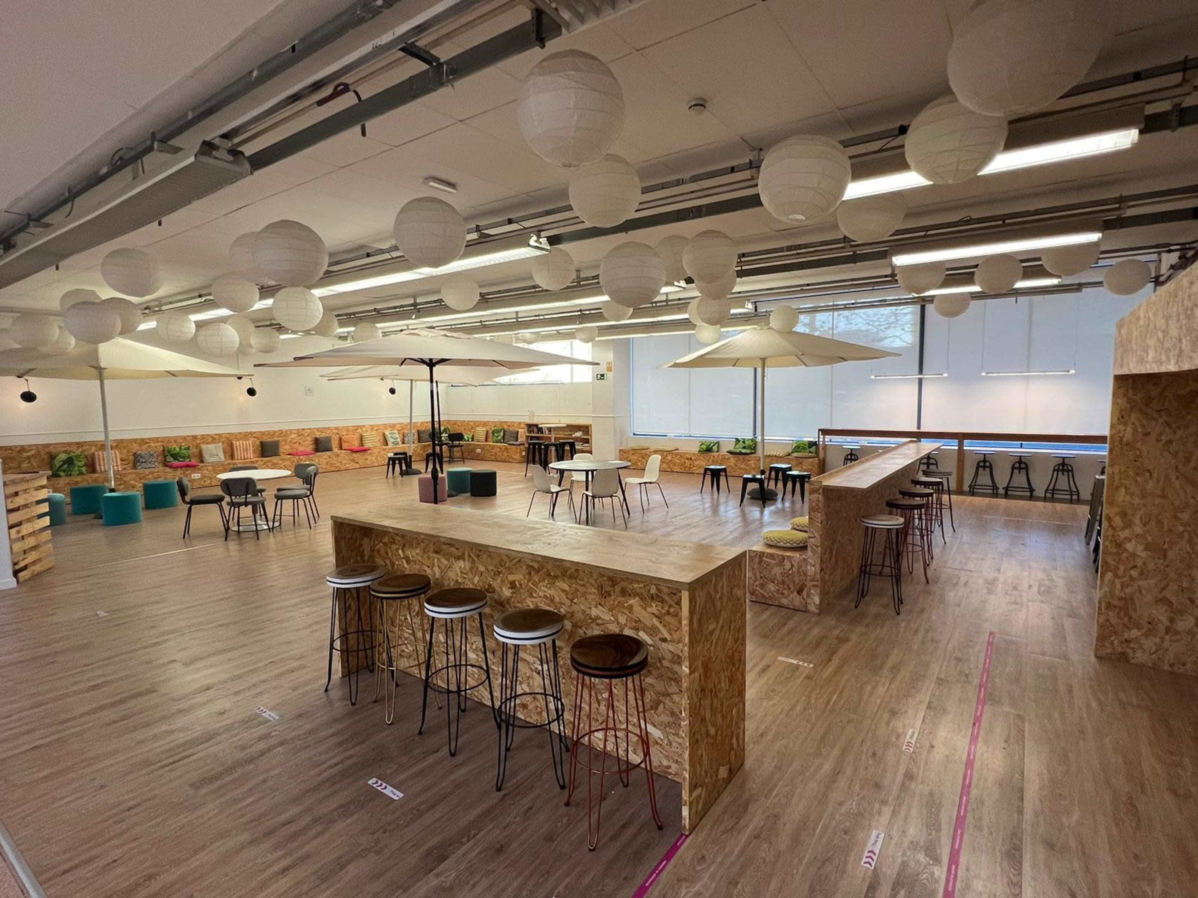 A spacious indoor workspace with wooden flooring, arranged seating areas, and hanging paper lanterns.