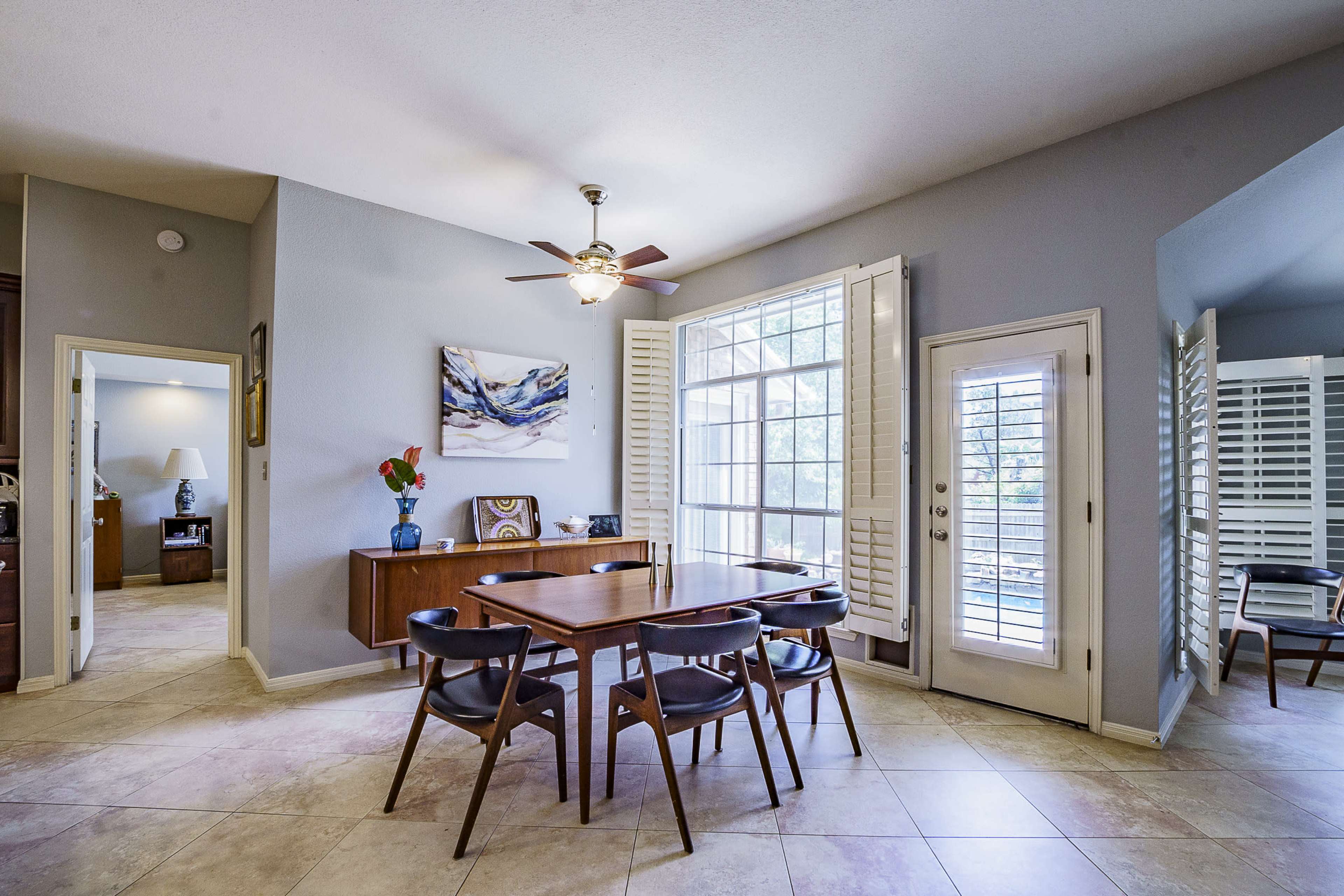 A dining area features a wooden table surrounded by black chairs, with a large window and a door leading to an outdoor space.