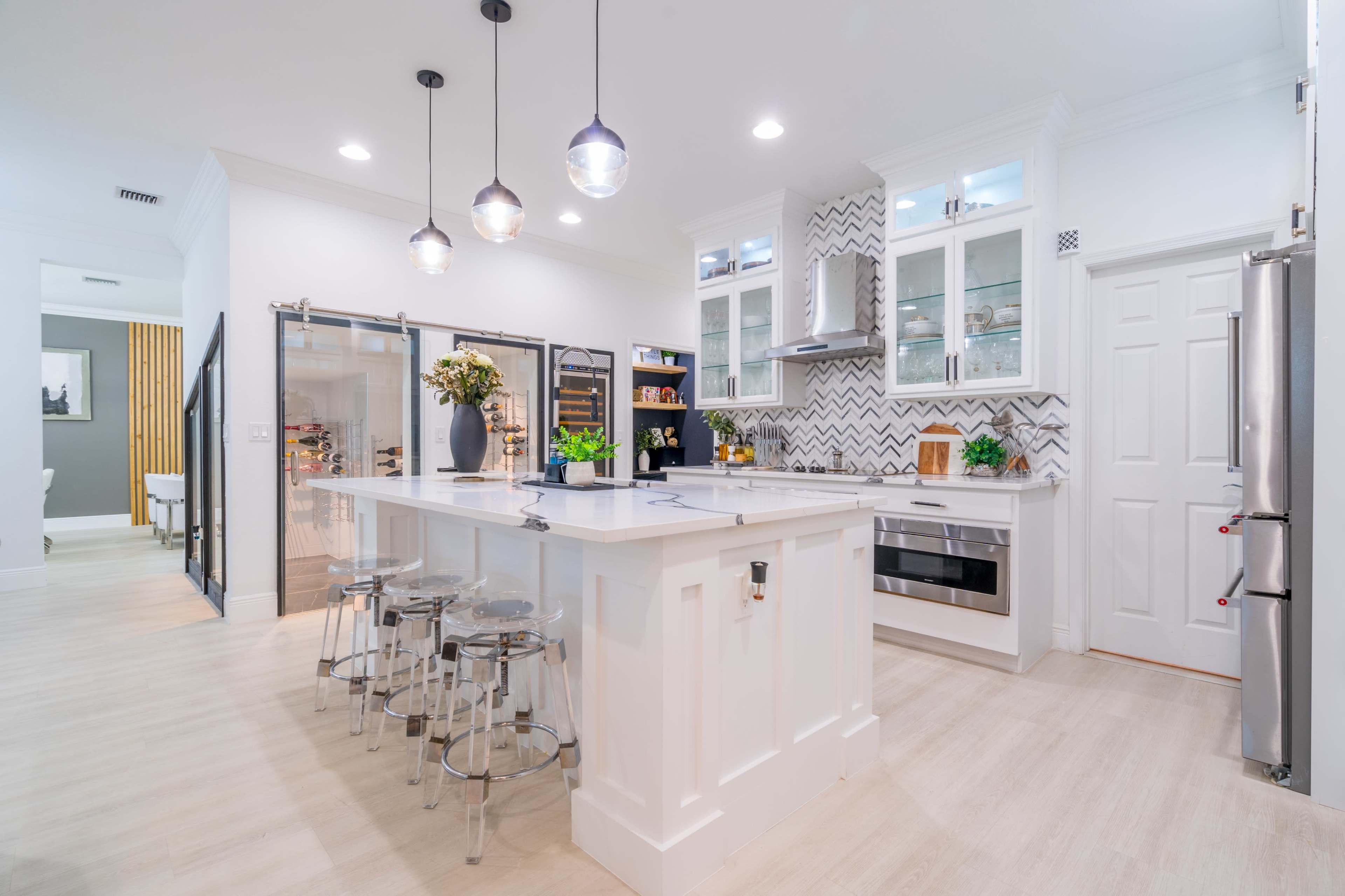 A modern kitchen features an island with bar stools, sleek cabinetry, and pendant lighting above.