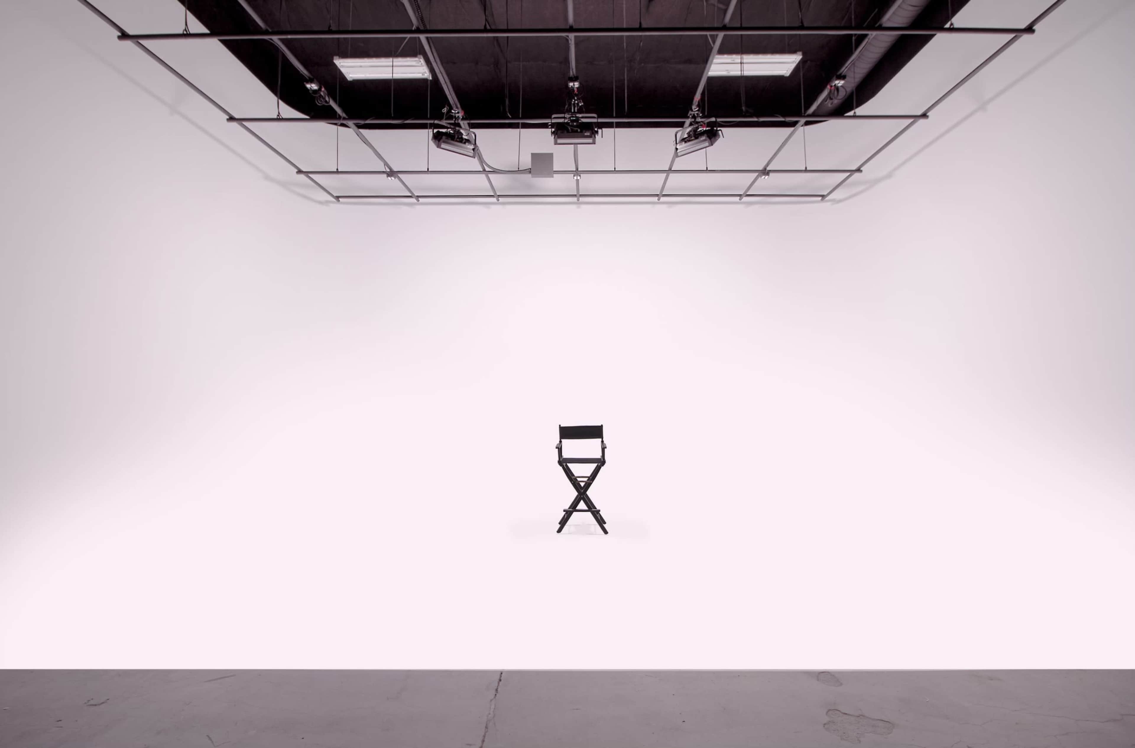 A single black director's chair is positioned in the center of a spacious, empty white studio.