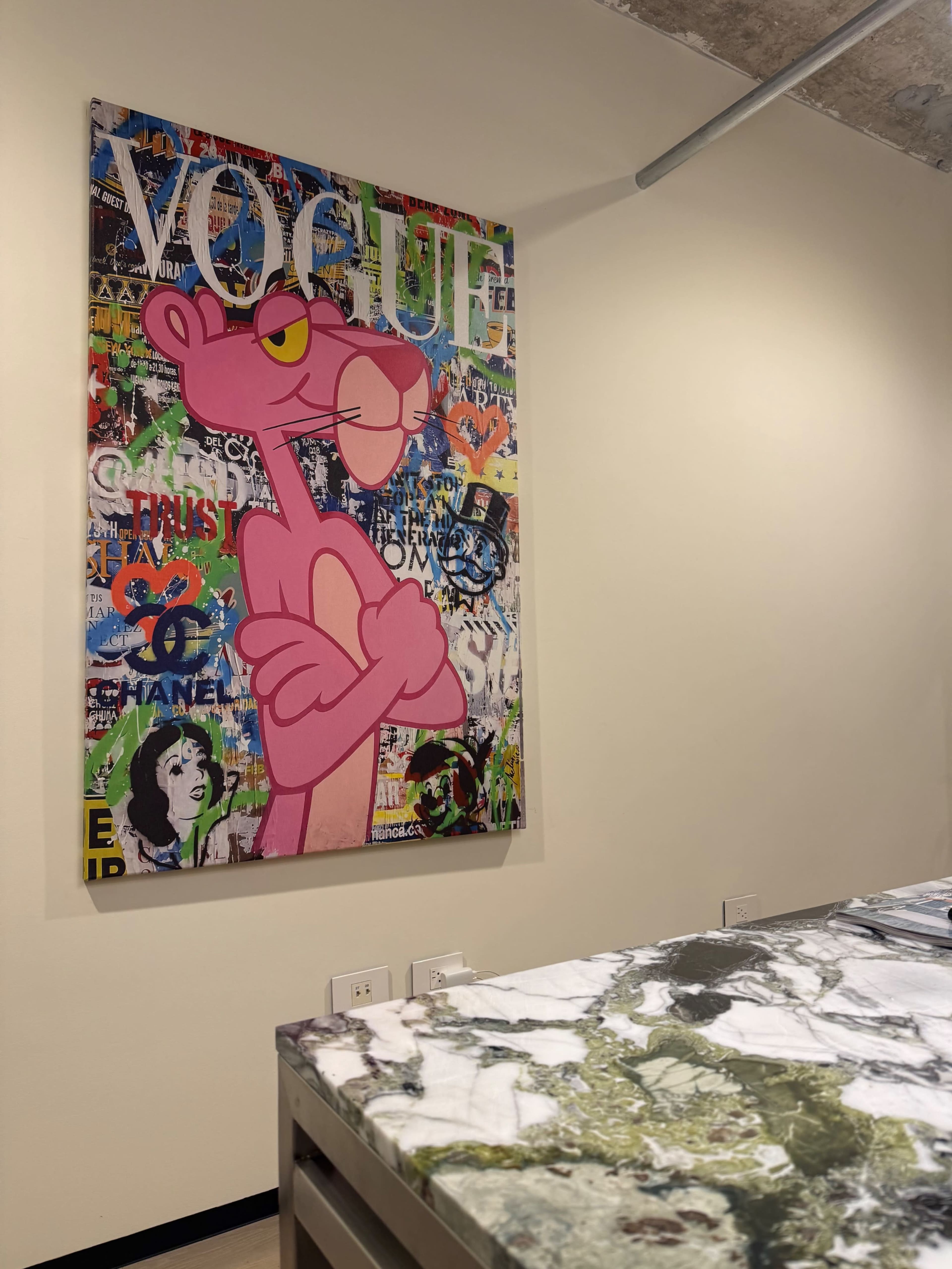 The image shows a modern interior with a colorful painting of a pink panther featuring the word "VOGUE" and other graffiti-like elements on the wall beside a marble countertop.