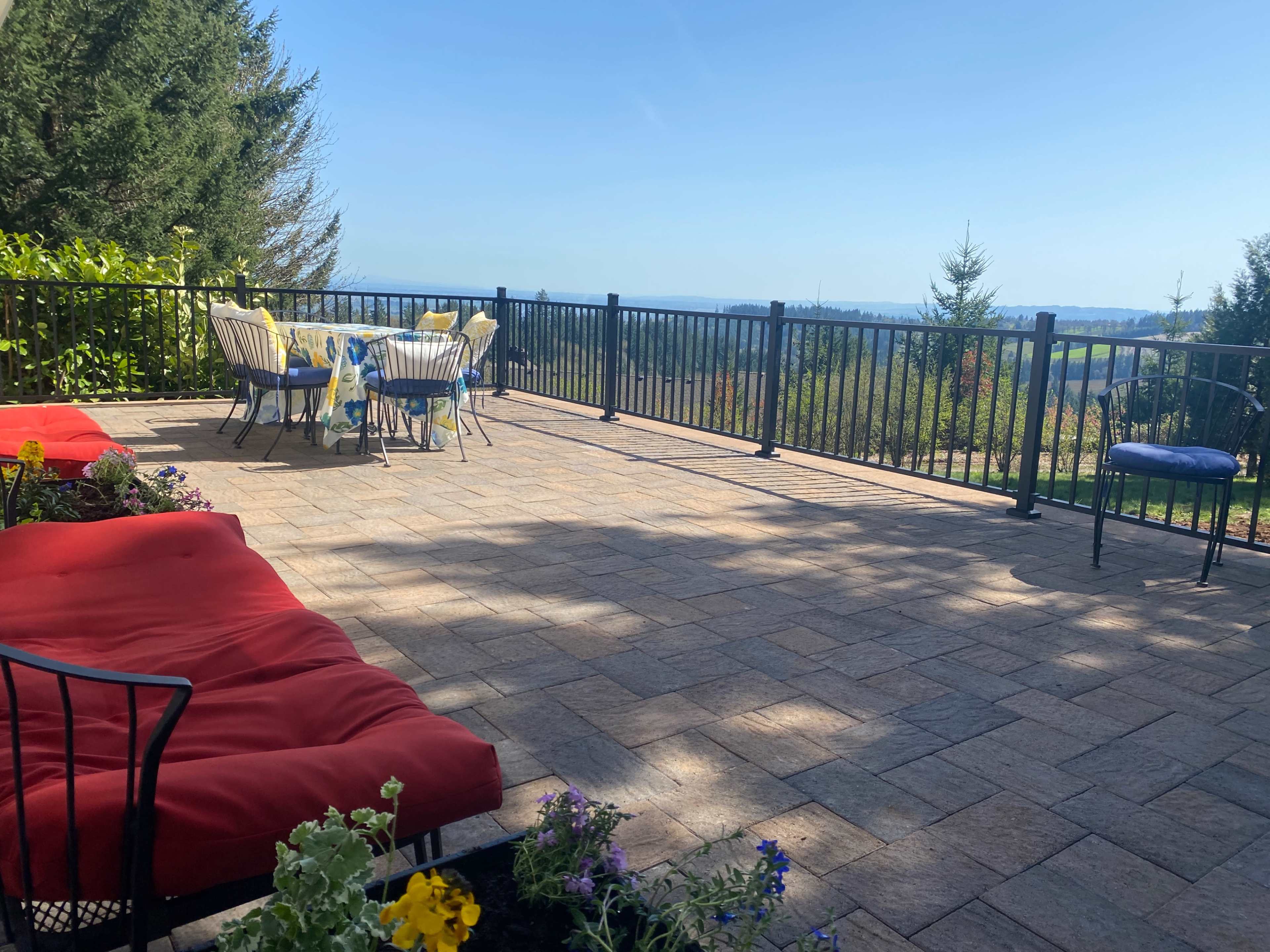 A patio with red lounge chairs and a table set for dining overlooks a scenic view of trees and hills.