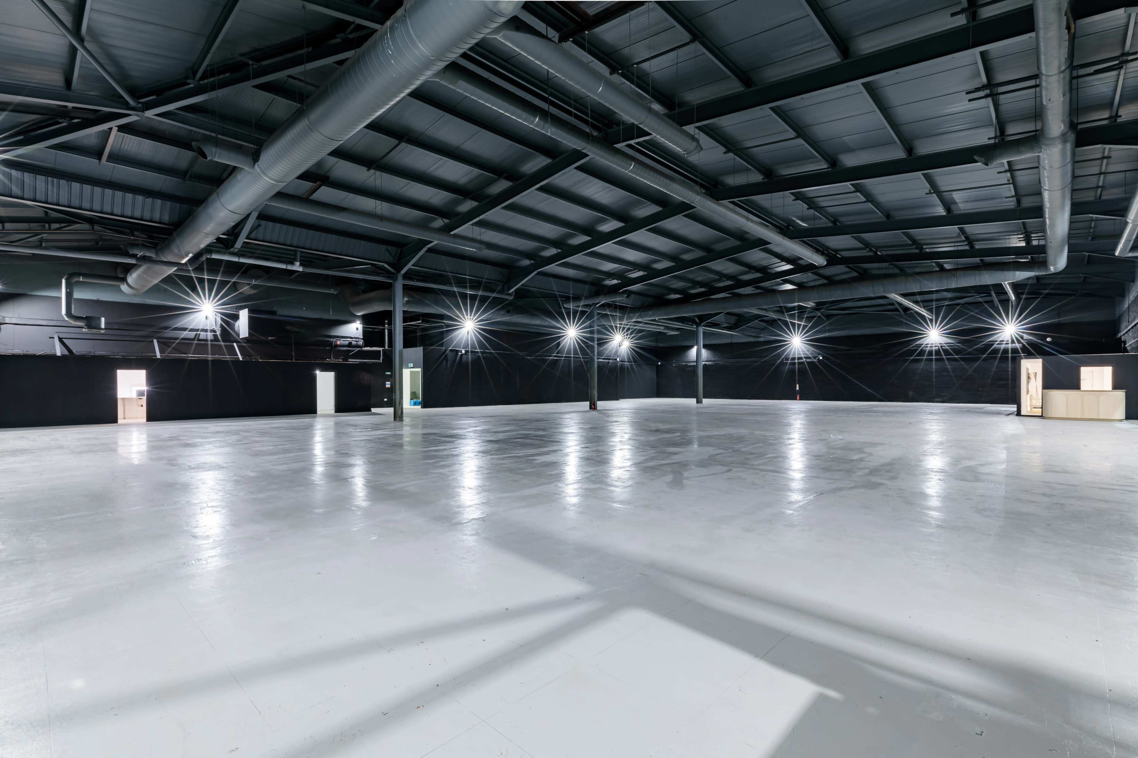 The image shows a large, empty industrial space with a high ceiling and overhead lighting.