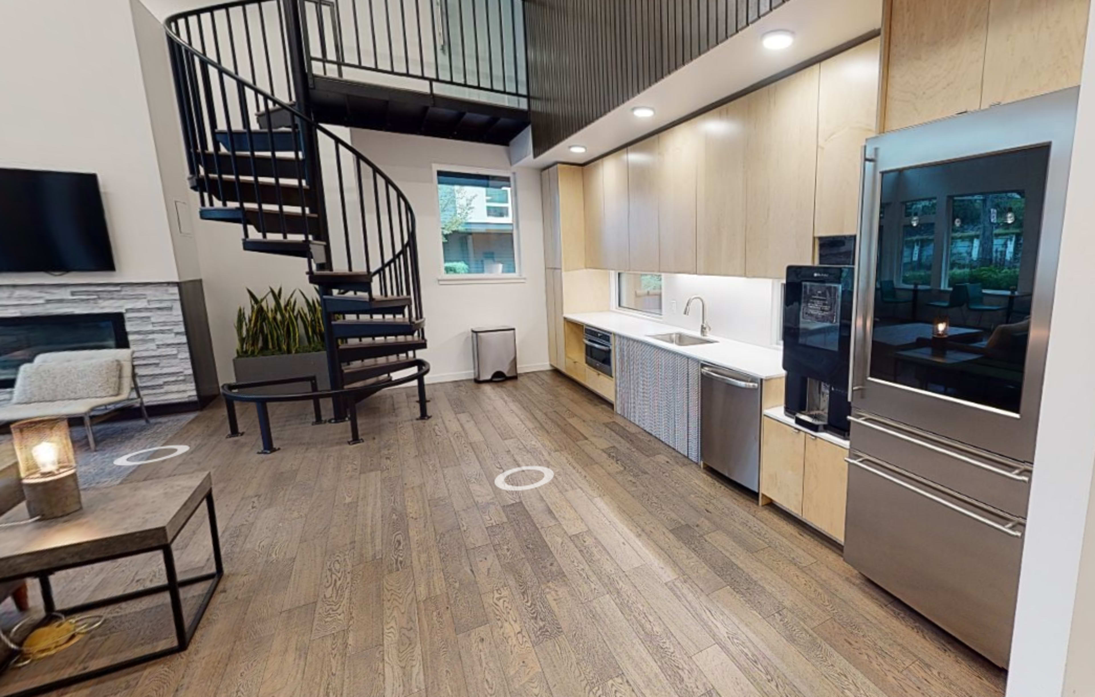 A modern kitchen with a spiral staircase leading to an upper level, featuring wood flooring and stainless steel appliances.