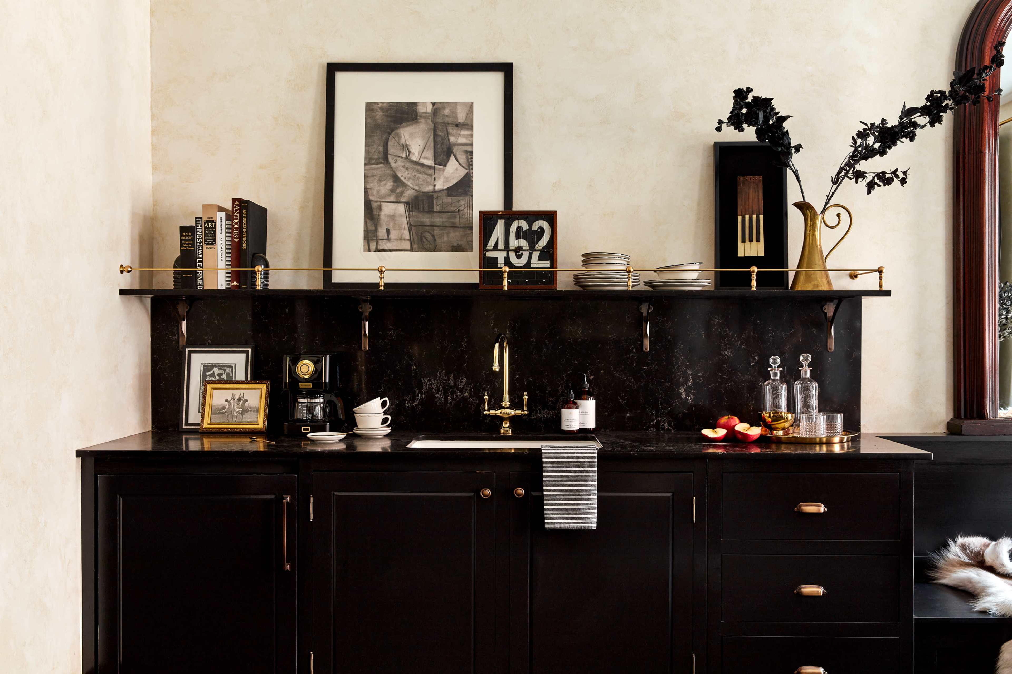 A black kitchen counter with a coffee maker, decorative items, and a wall shelf displaying books and a framed artwork.