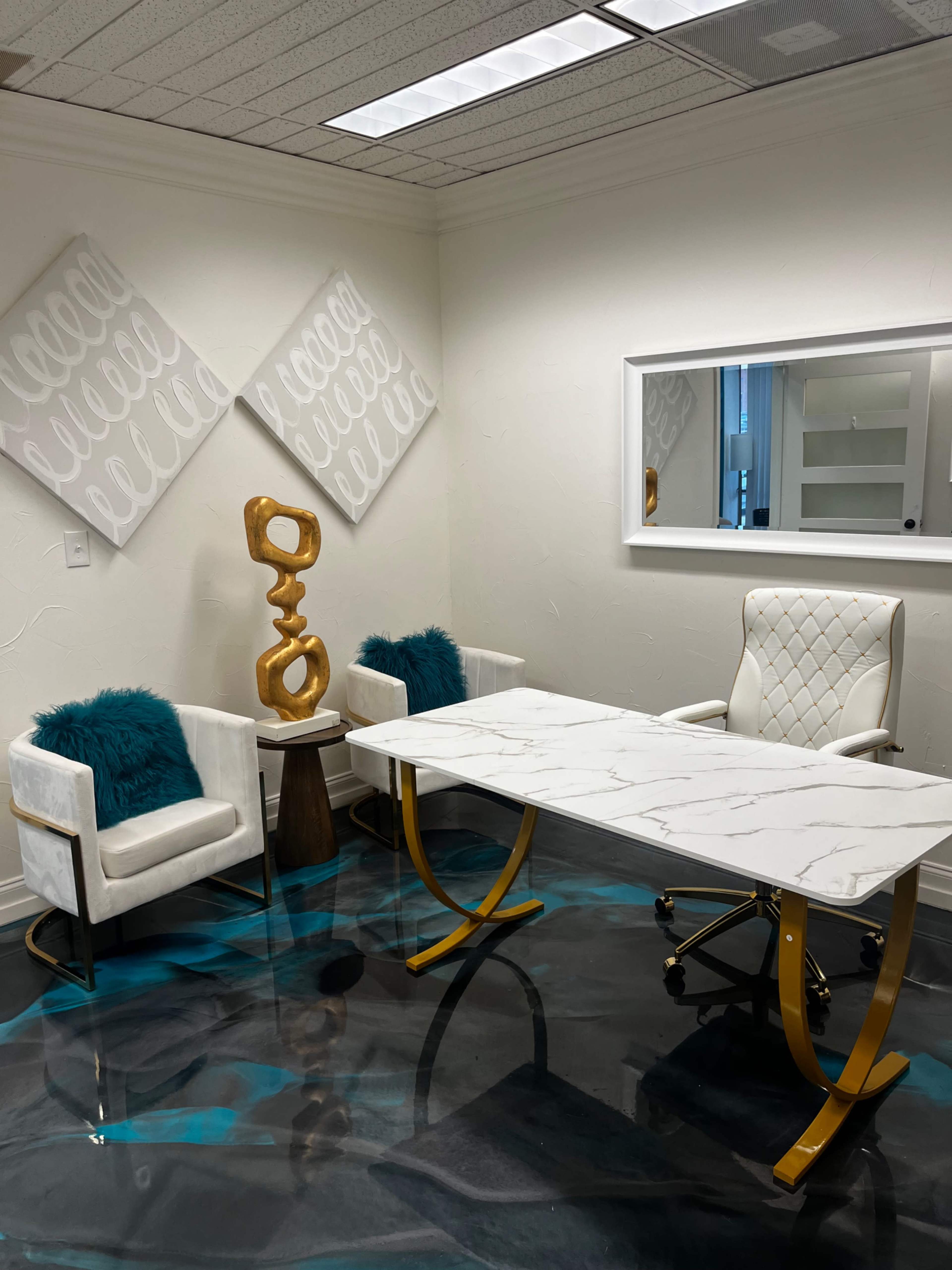 The image showcases a modern office space featuring a marble-topped desk, two white chairs with teal accents, and a decorative wooden sculpture against a backdrop of light-colored walls.