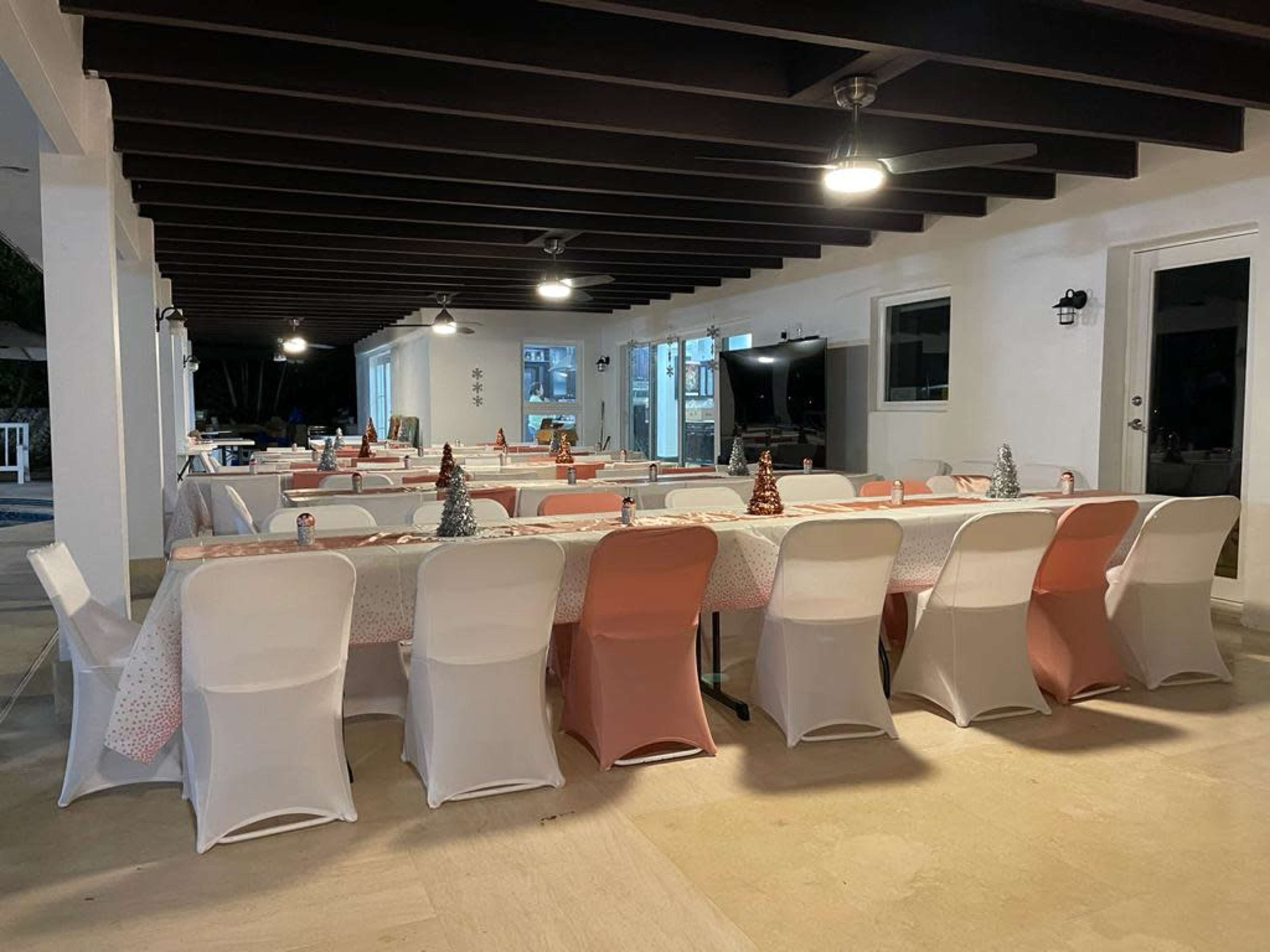A large dining area is set up with multiple tables covered in tablecloths and adorned with small decorative trees.