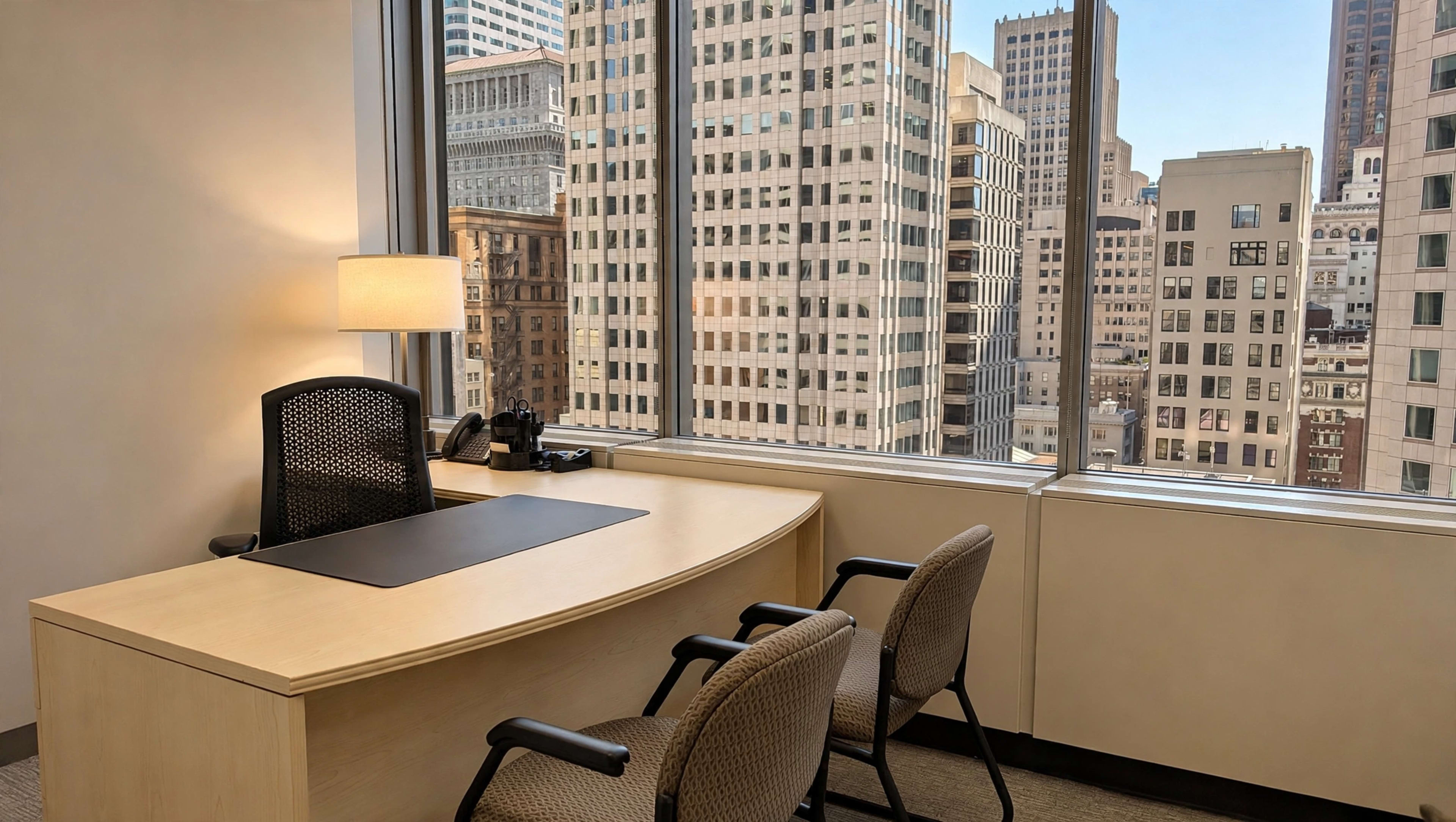 A modern office features a curved desk, two chairs, a lamp, and large windows displaying a cityscape.
