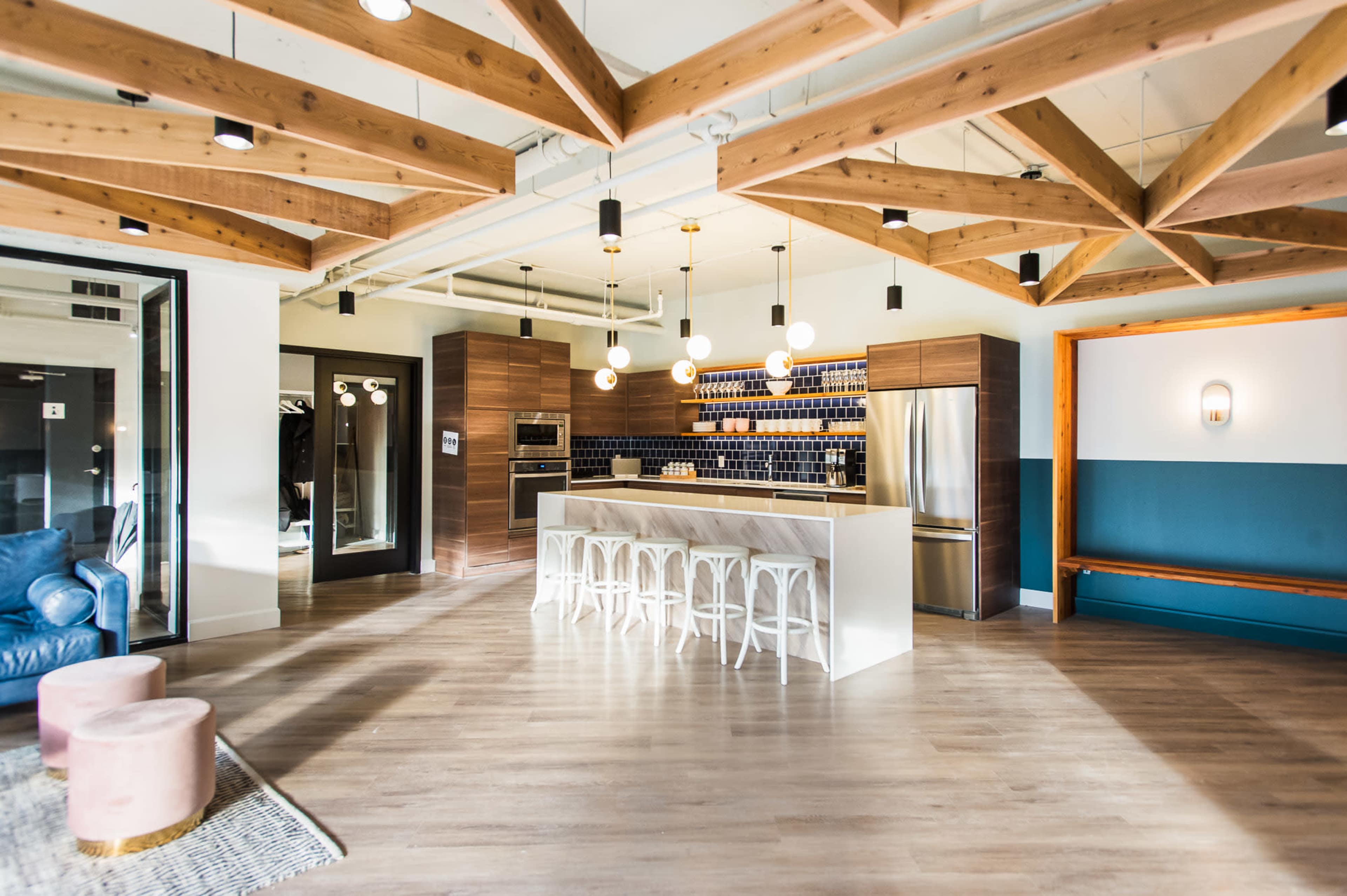 A modern kitchen features a central island with seating, surrounded by wood-beamed ceilings and sleek cabinetry.