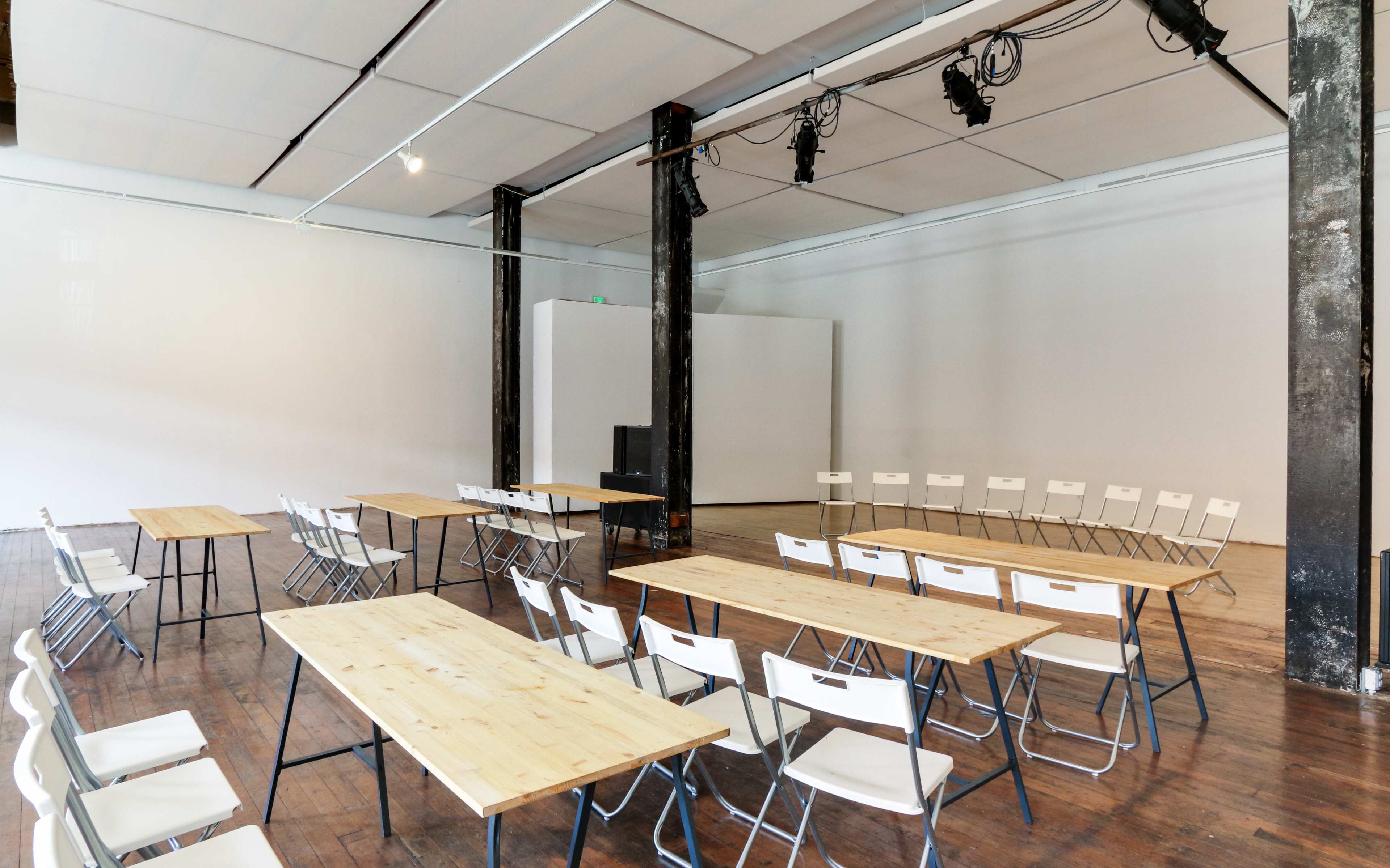 A spacious room features several rows of wooden tables and white folding chairs arranged for a meeting or event.