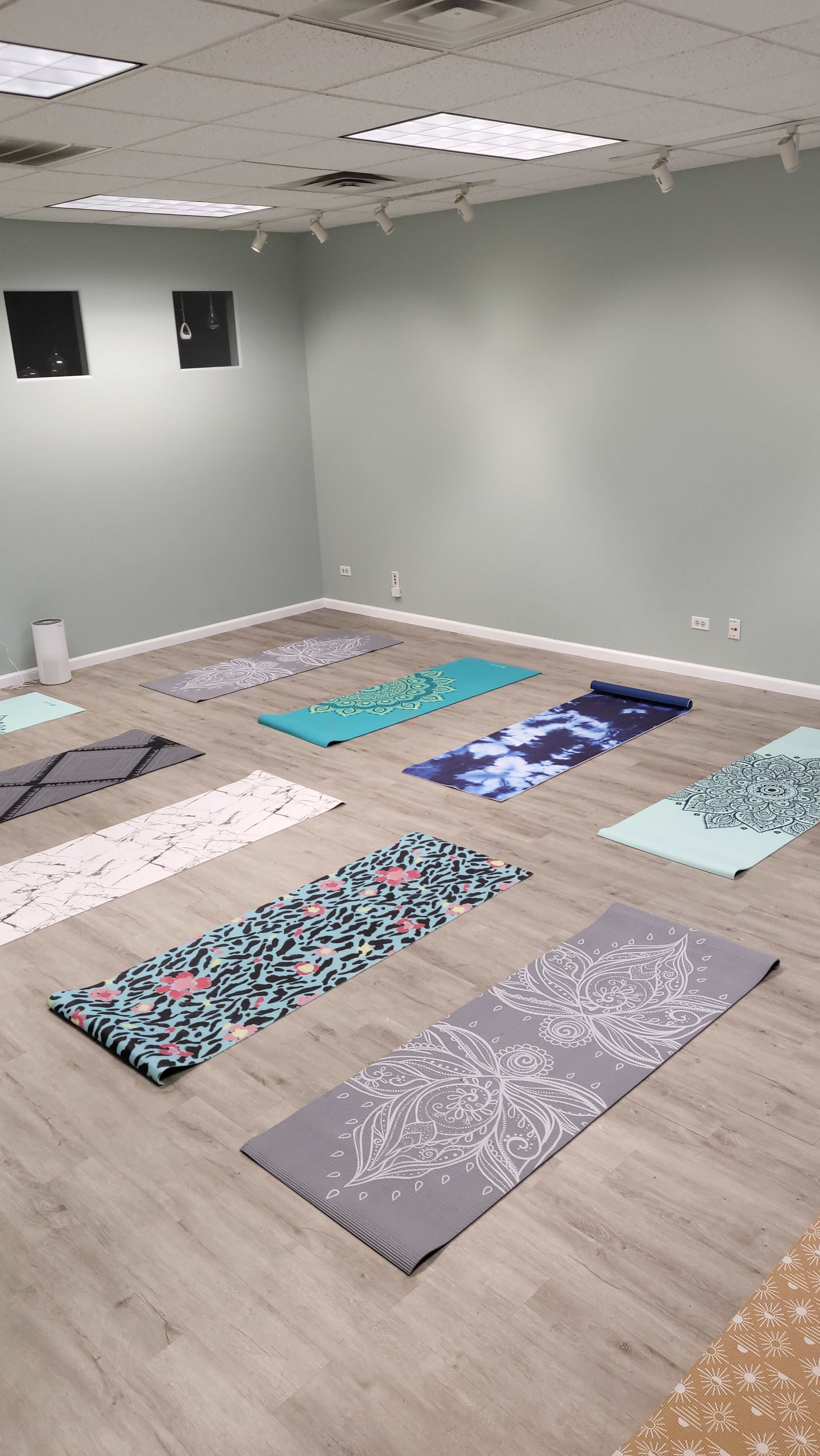 The image shows a quiet yoga studio with multiple yoga mats arranged in a grid pattern on a wooden floor, surrounded by pale green walls.