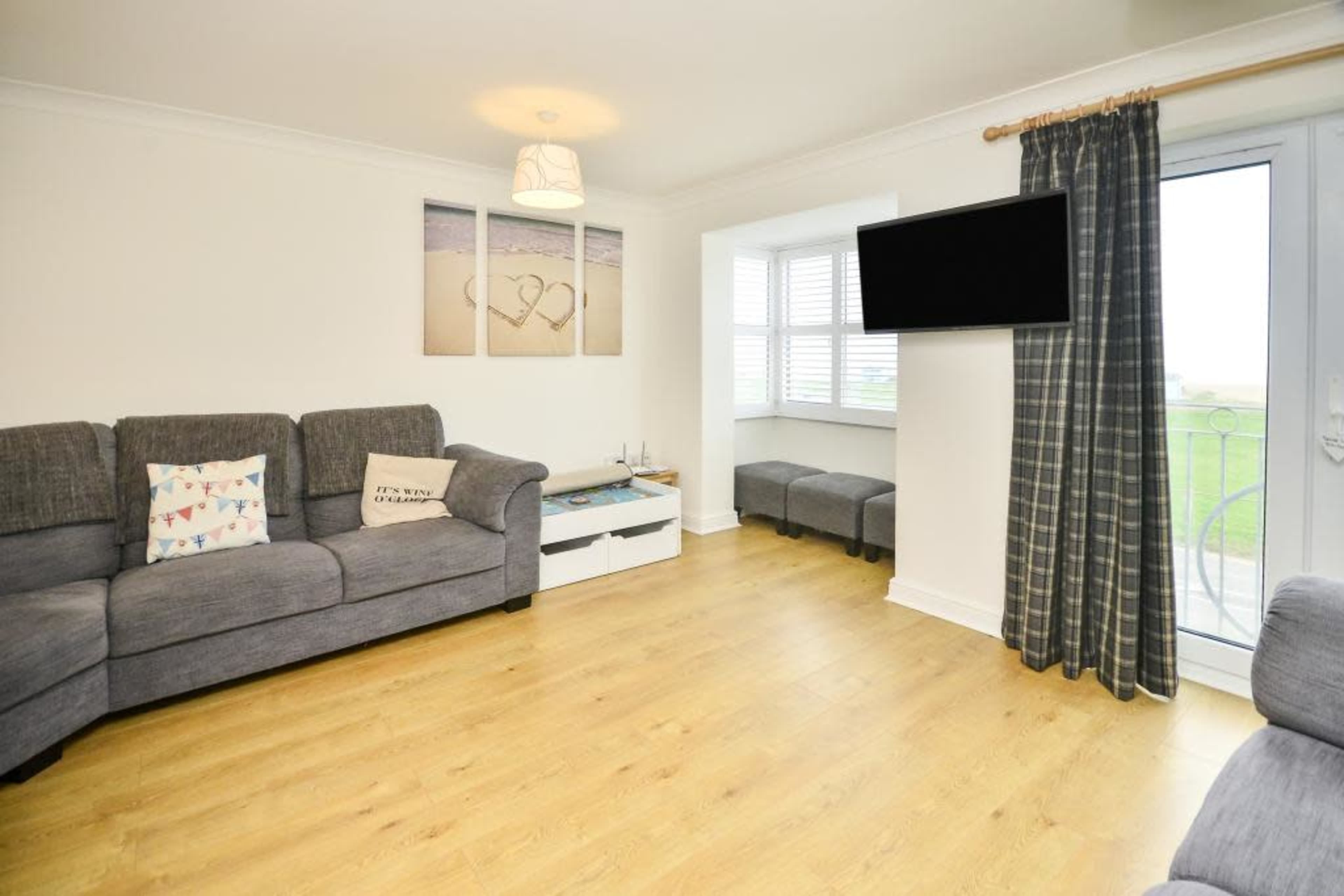 A cozy living room with a gray sectional sofa, a coffee table, a TV mounted on the wall, and a door leading to a balcony.
