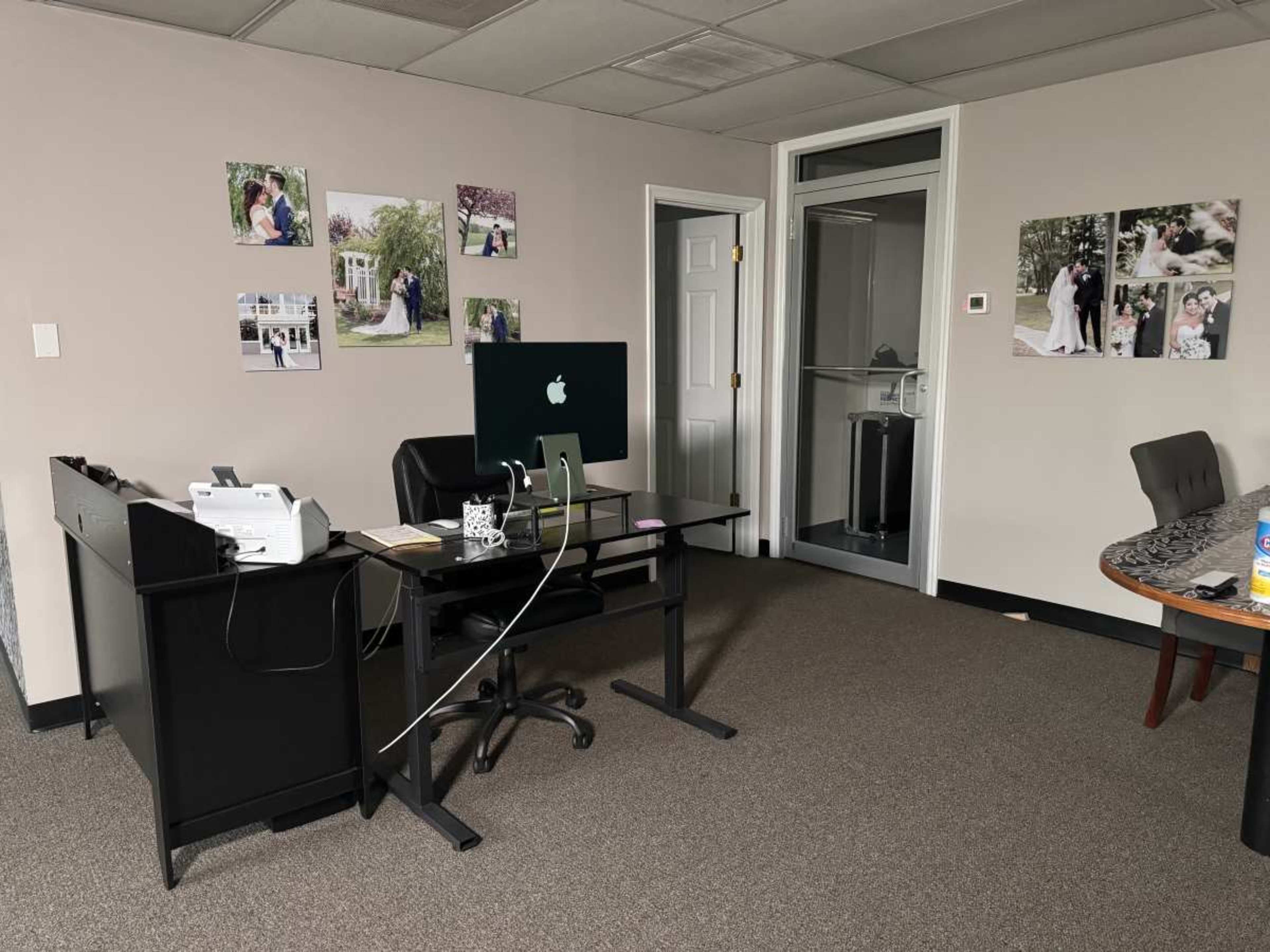 The image shows a spacious office with a desk, an iMac computer, a printer, and several framed photographs on the walls.