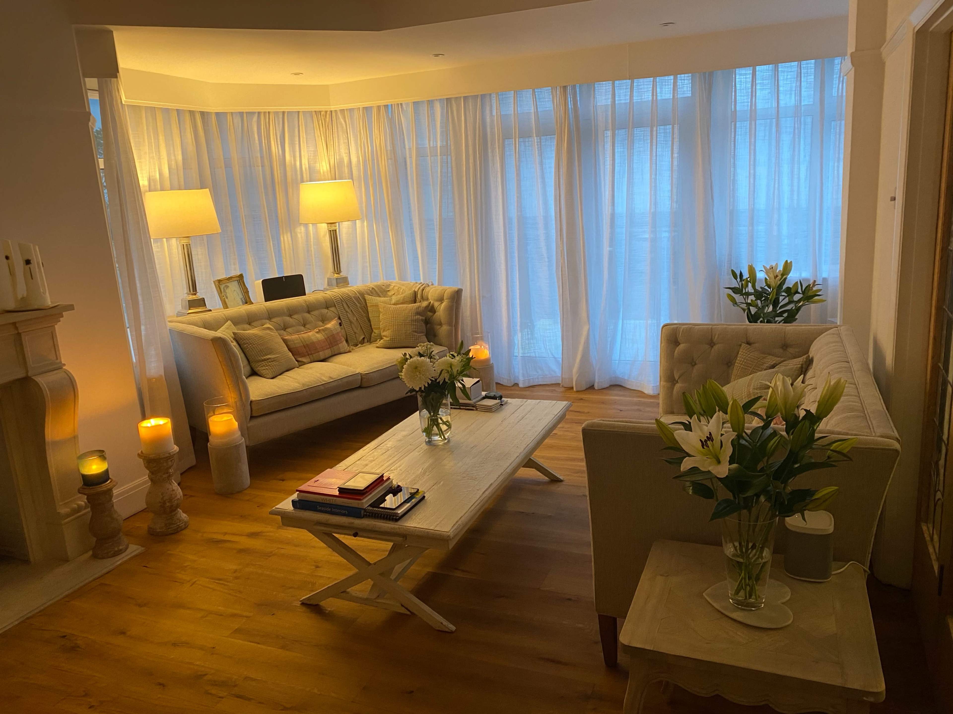The living room features two sofas, a coffee table, and decorative vases, all illuminated by soft lighting and surrounded by sheer curtains.
